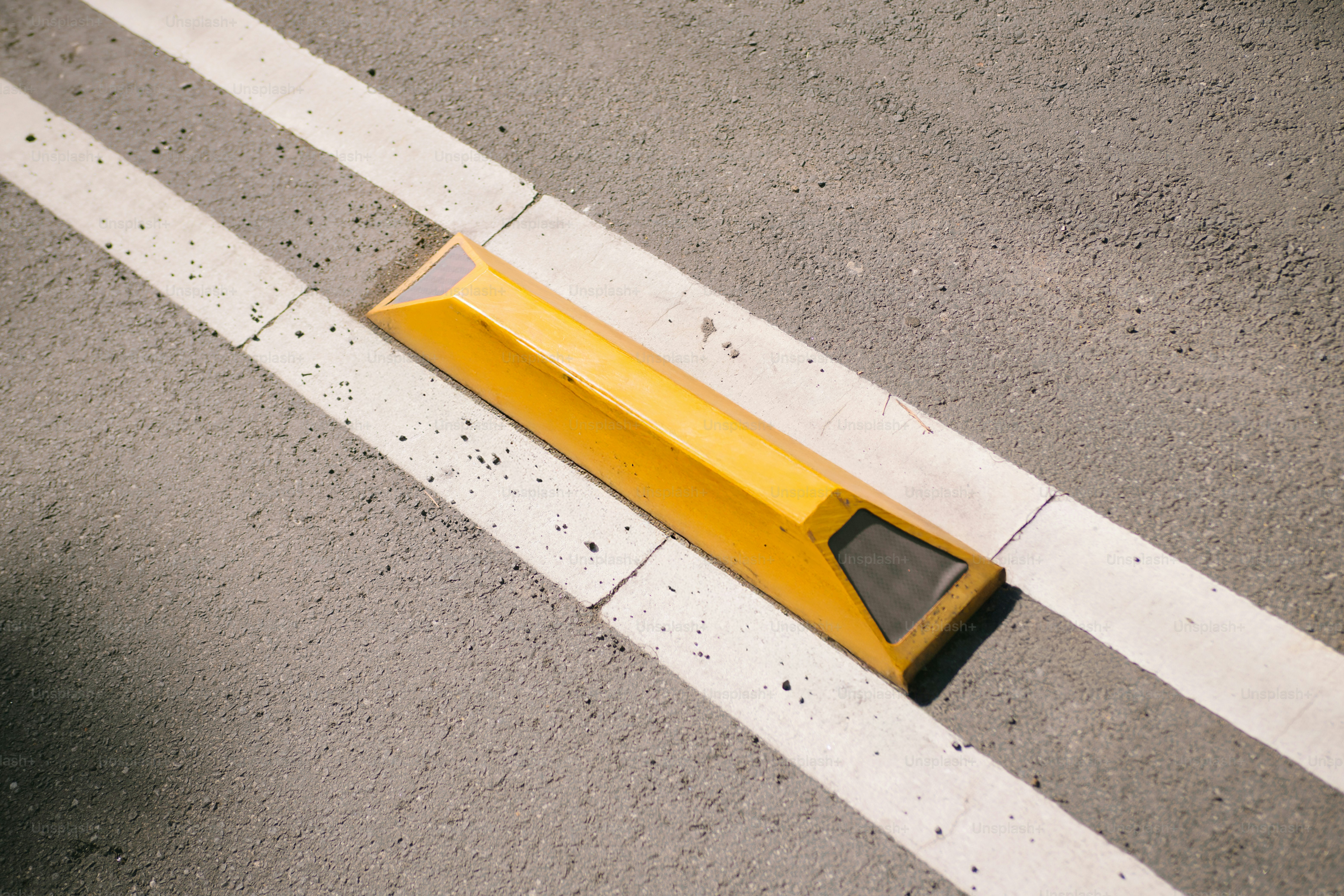 Réflecteur de route jaune entre des lignes blanches sur l’asphalte.