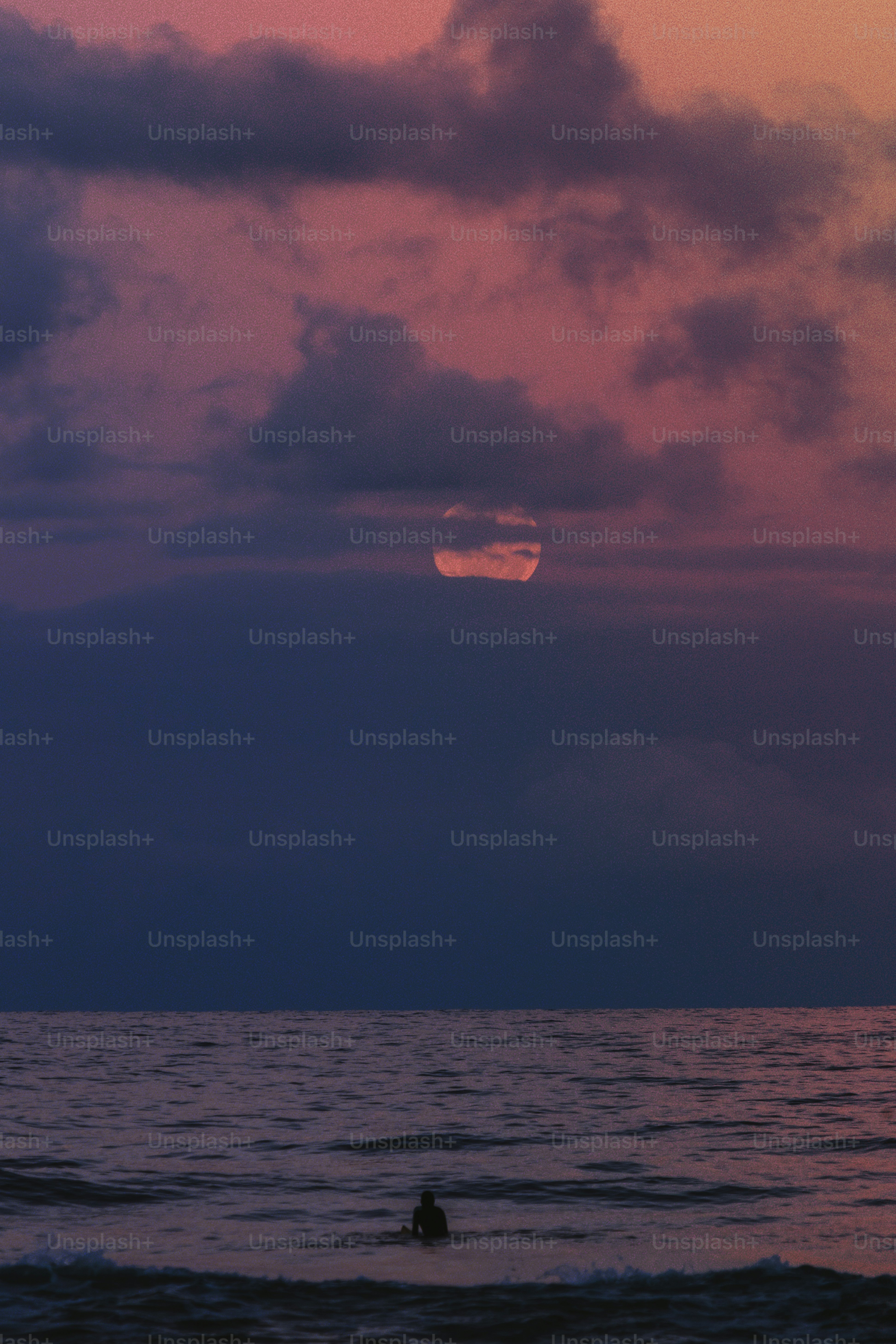 Surfer watches sunset through clouds over ocean