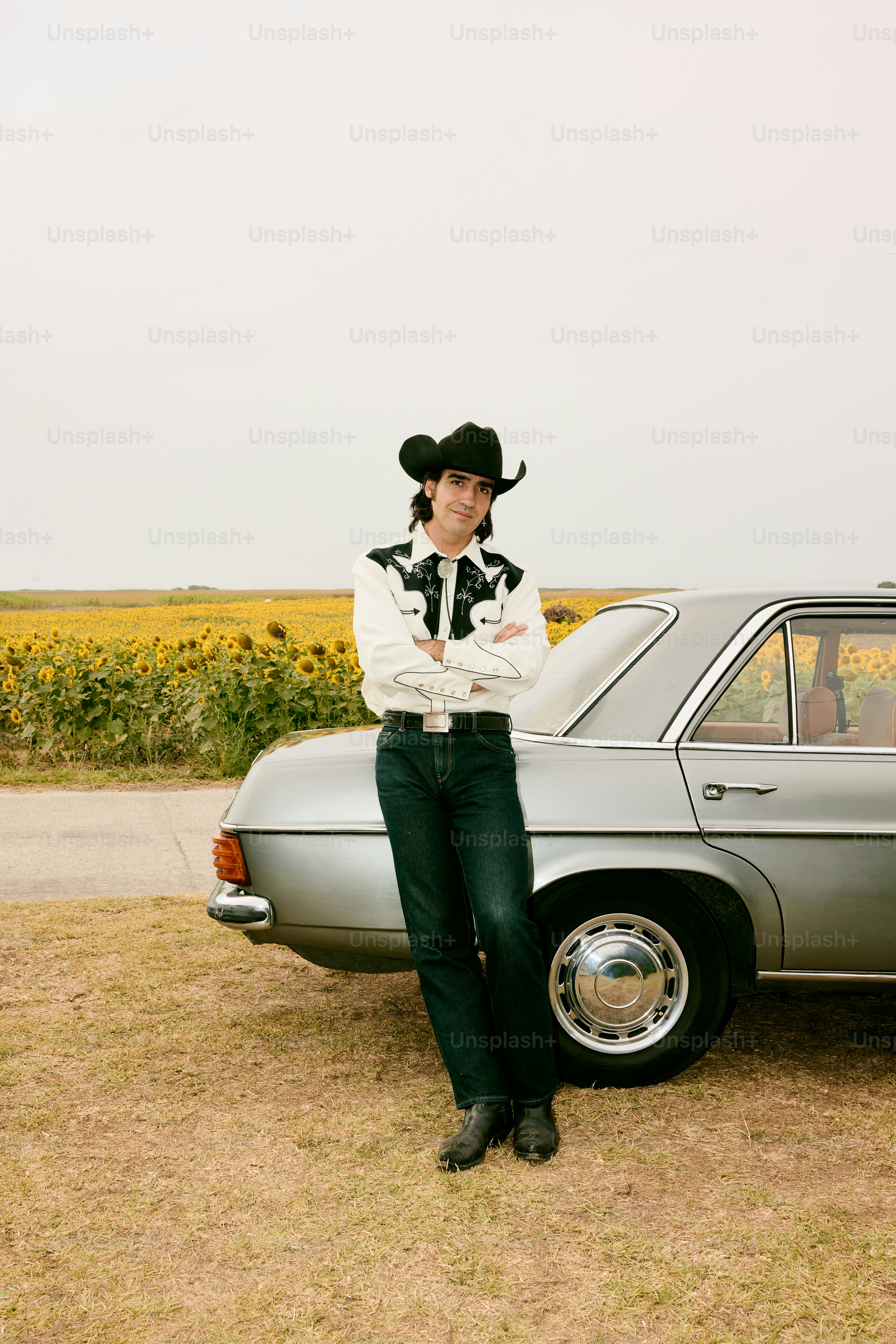 Man in cowboy hat leans on car by sunflower field