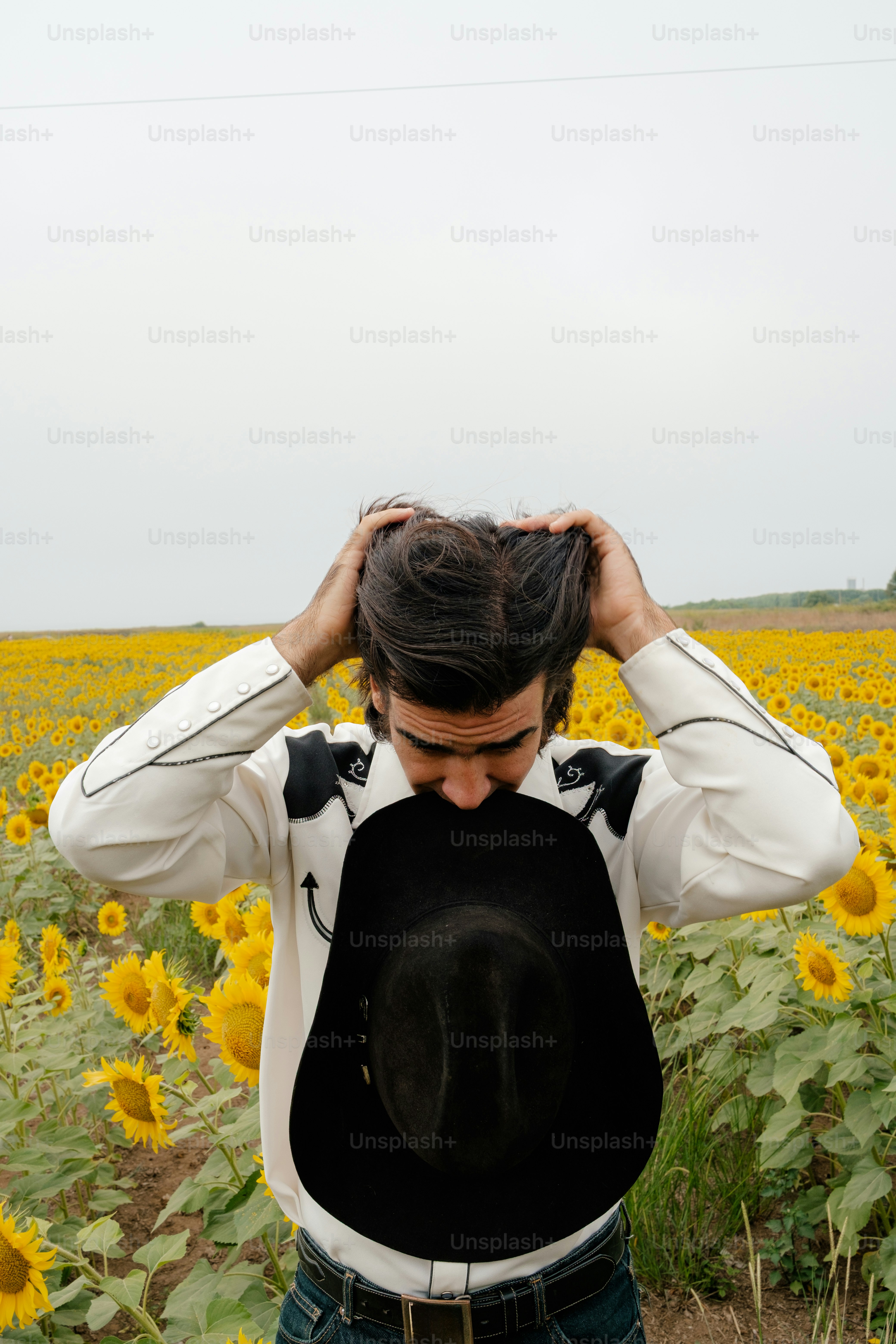 Man in cowboy shirt adjusting hat in sunflower field