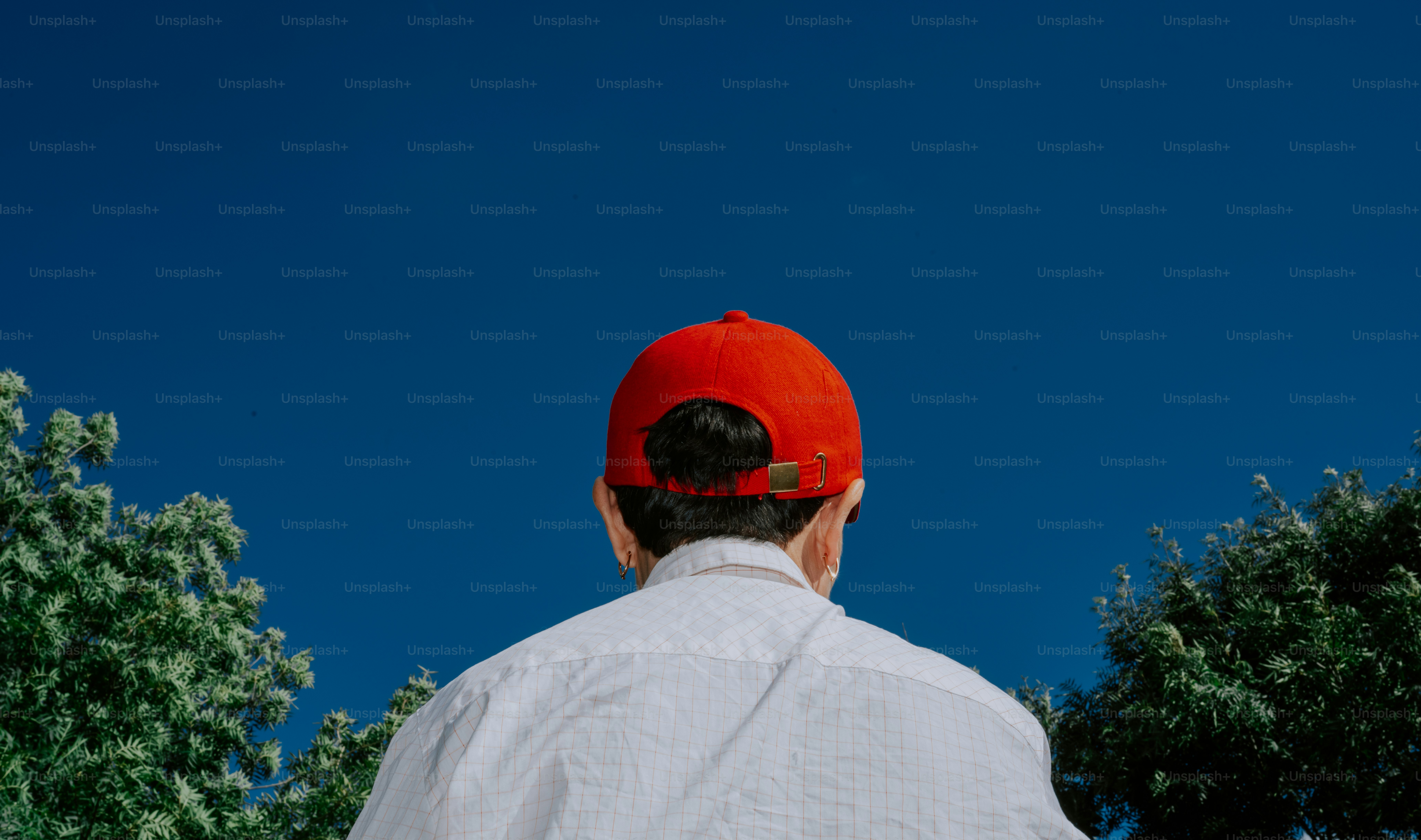 Man in red cap looks up at clear blue sky.
