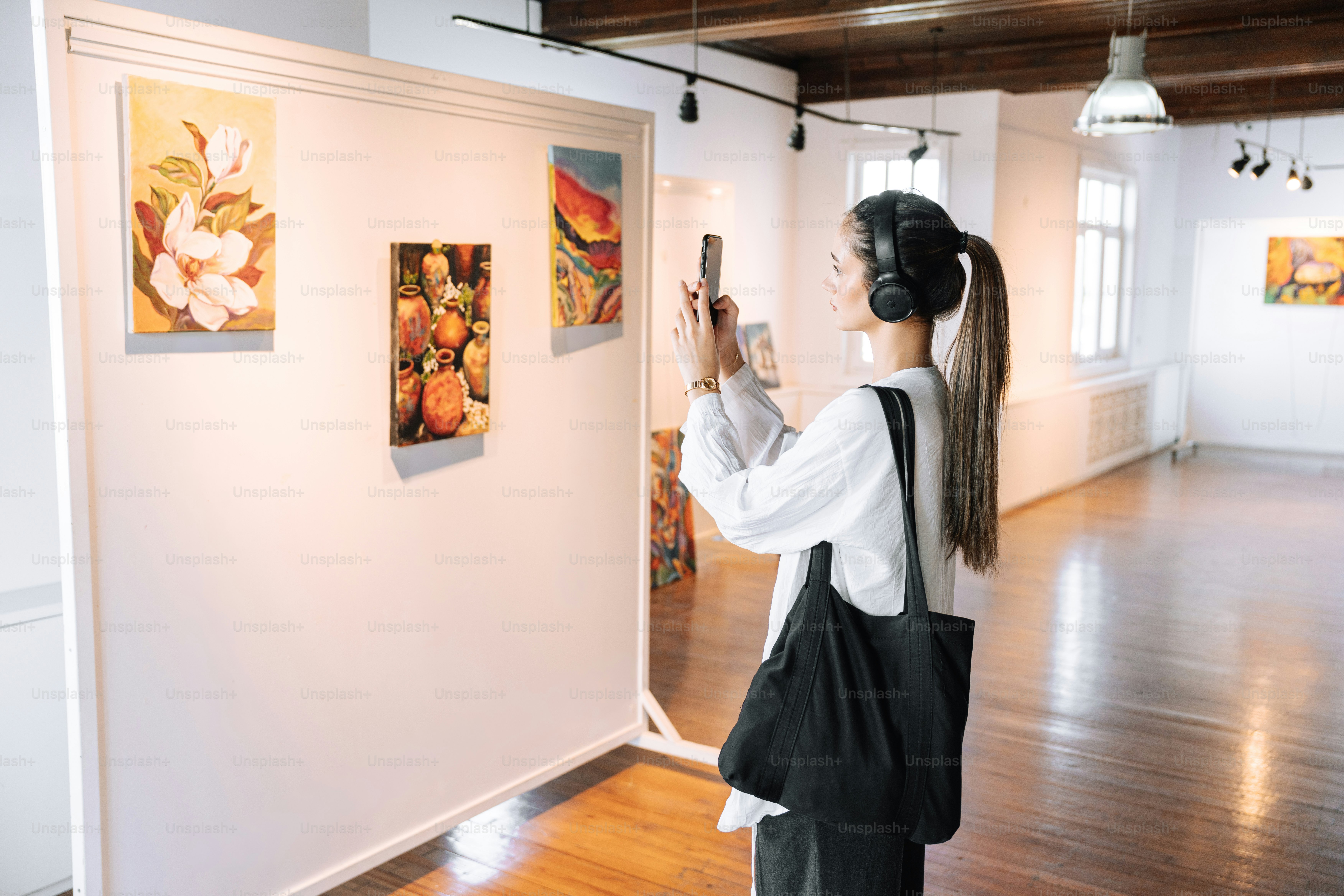 Woman photographs artwork in a bright art gallery.