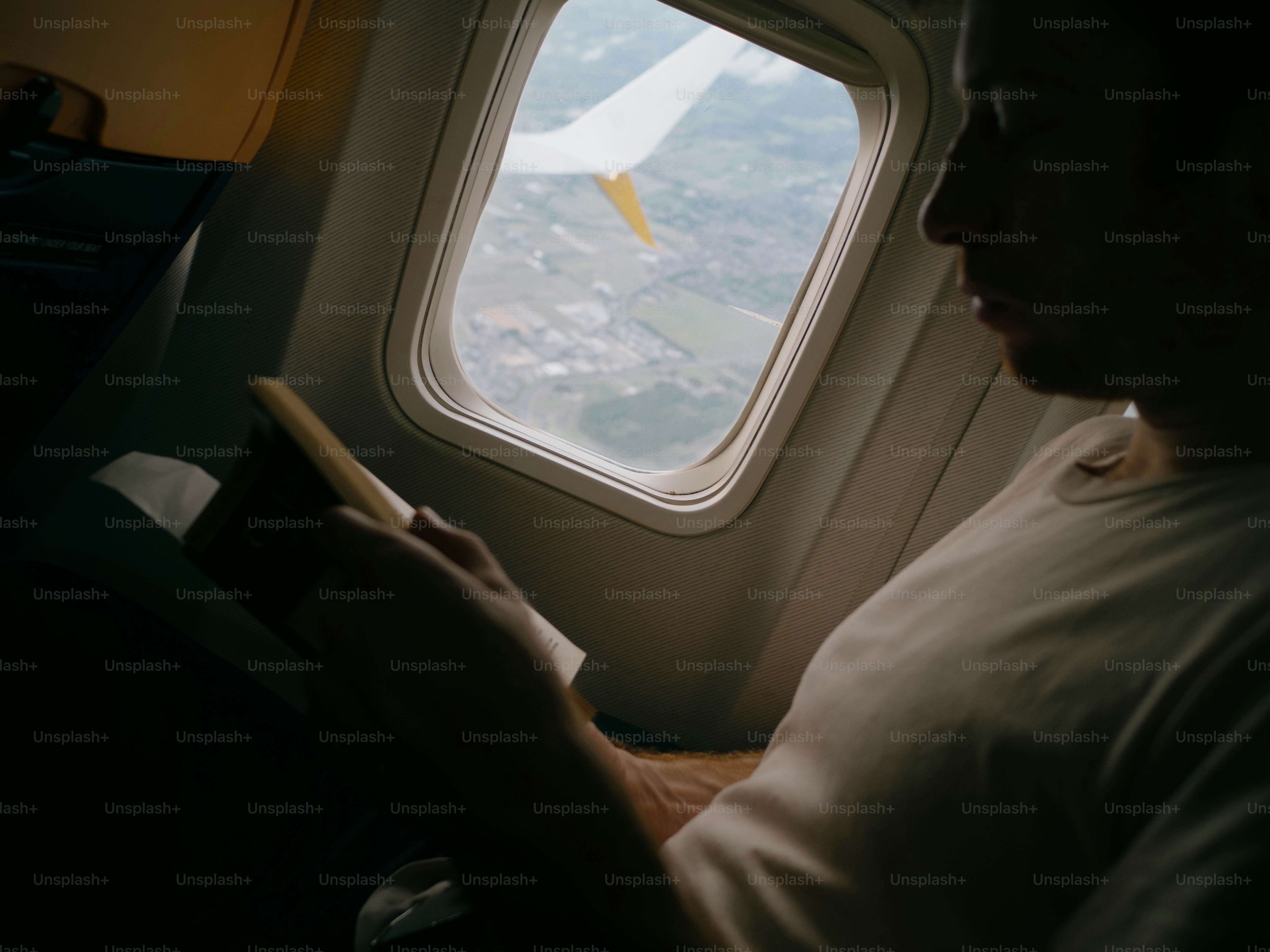 Man reading book inside airplane near window