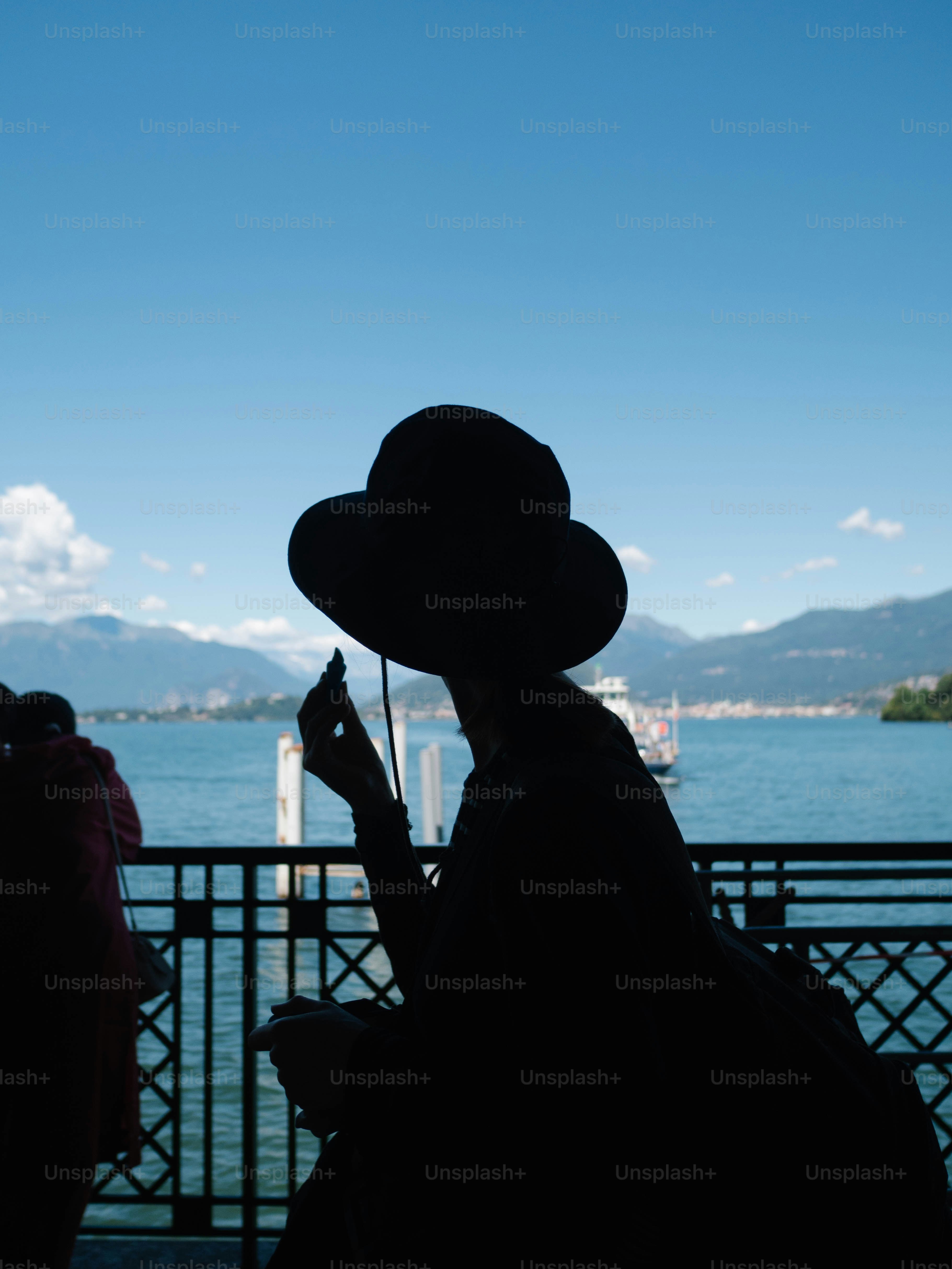 Silhouette of a woman wearing a hat by the water.