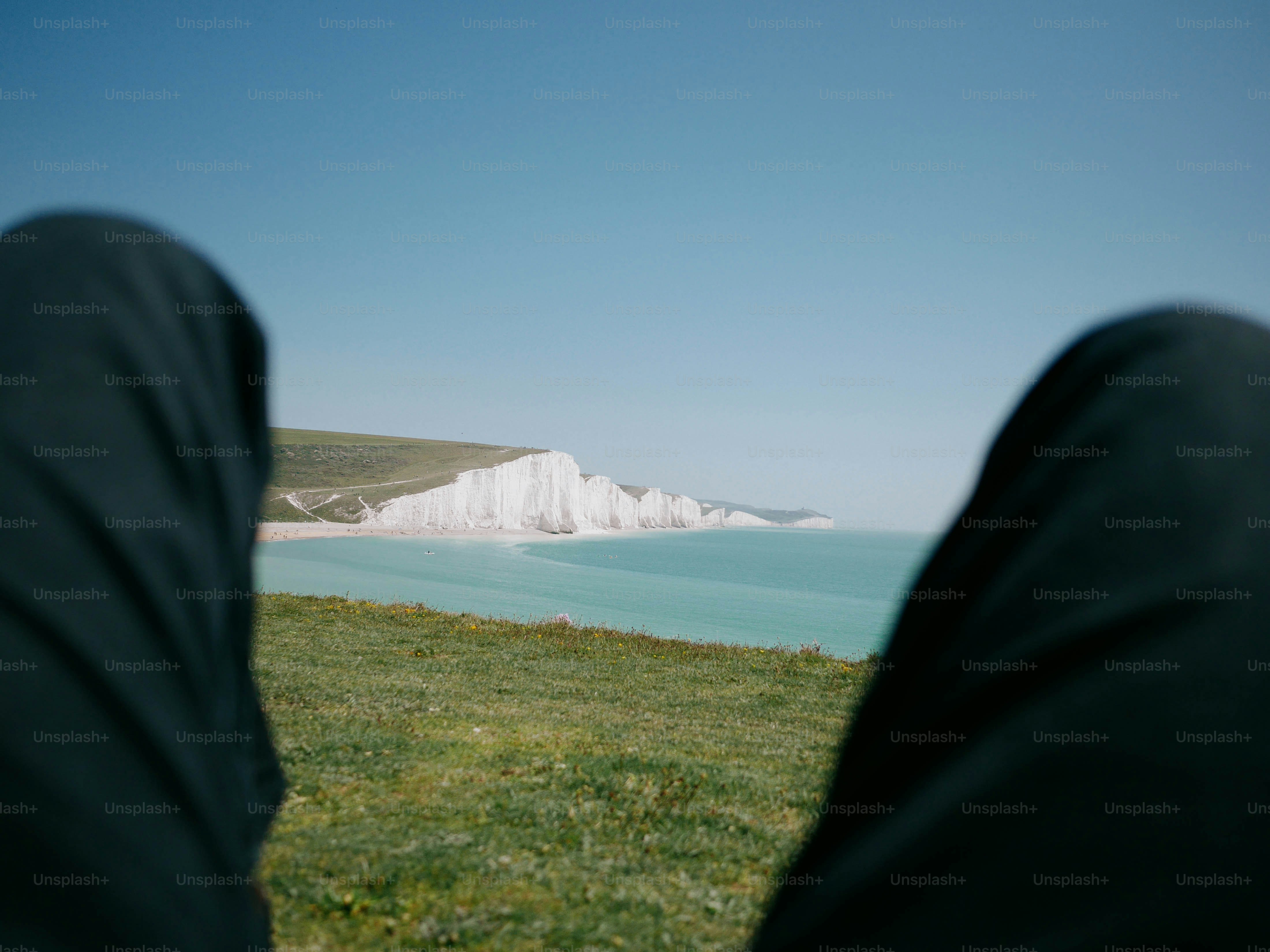Person sitting on grassy cliff overlooking white cliffs and ocean