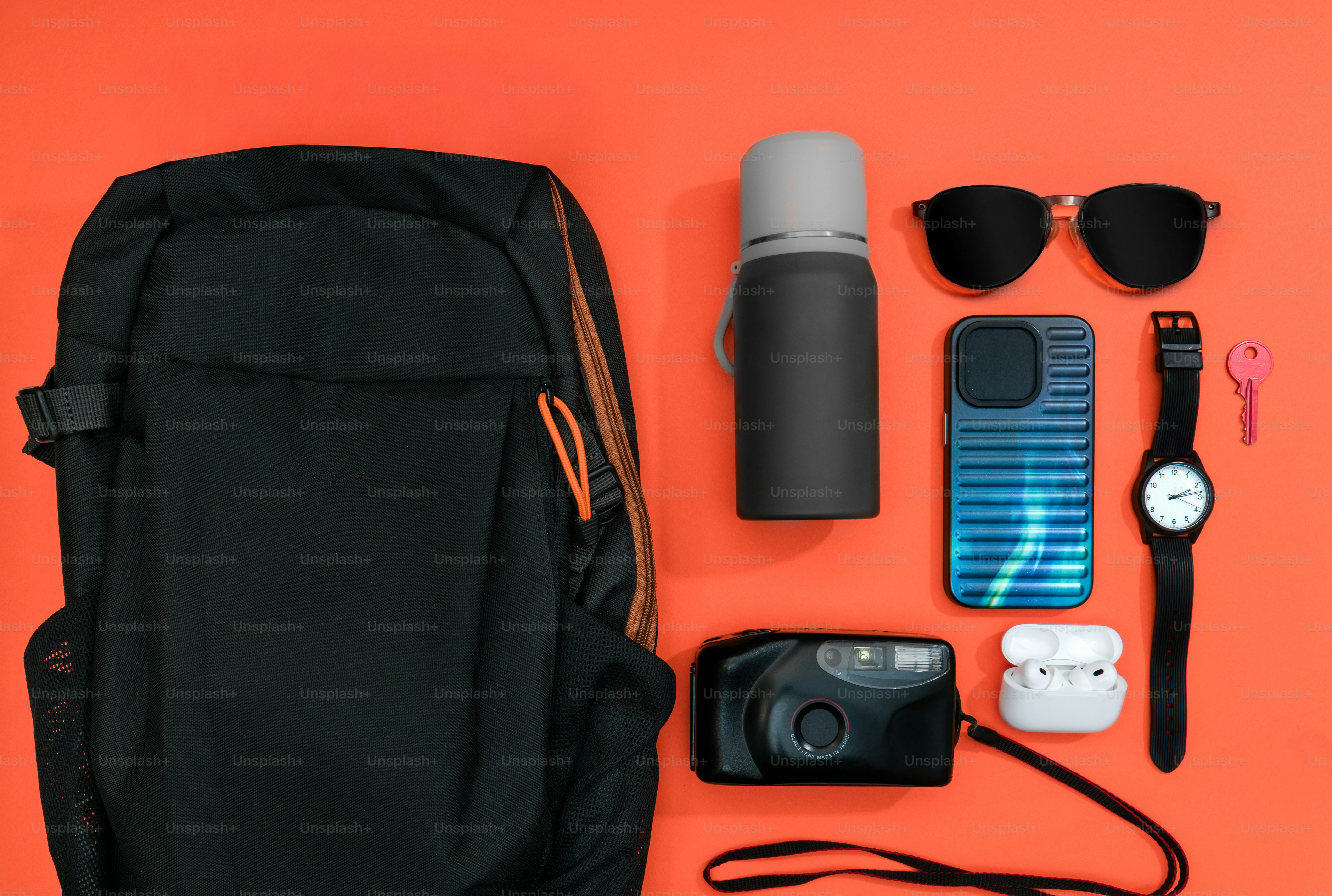 Black backpack with travel essentials arranged neatly.