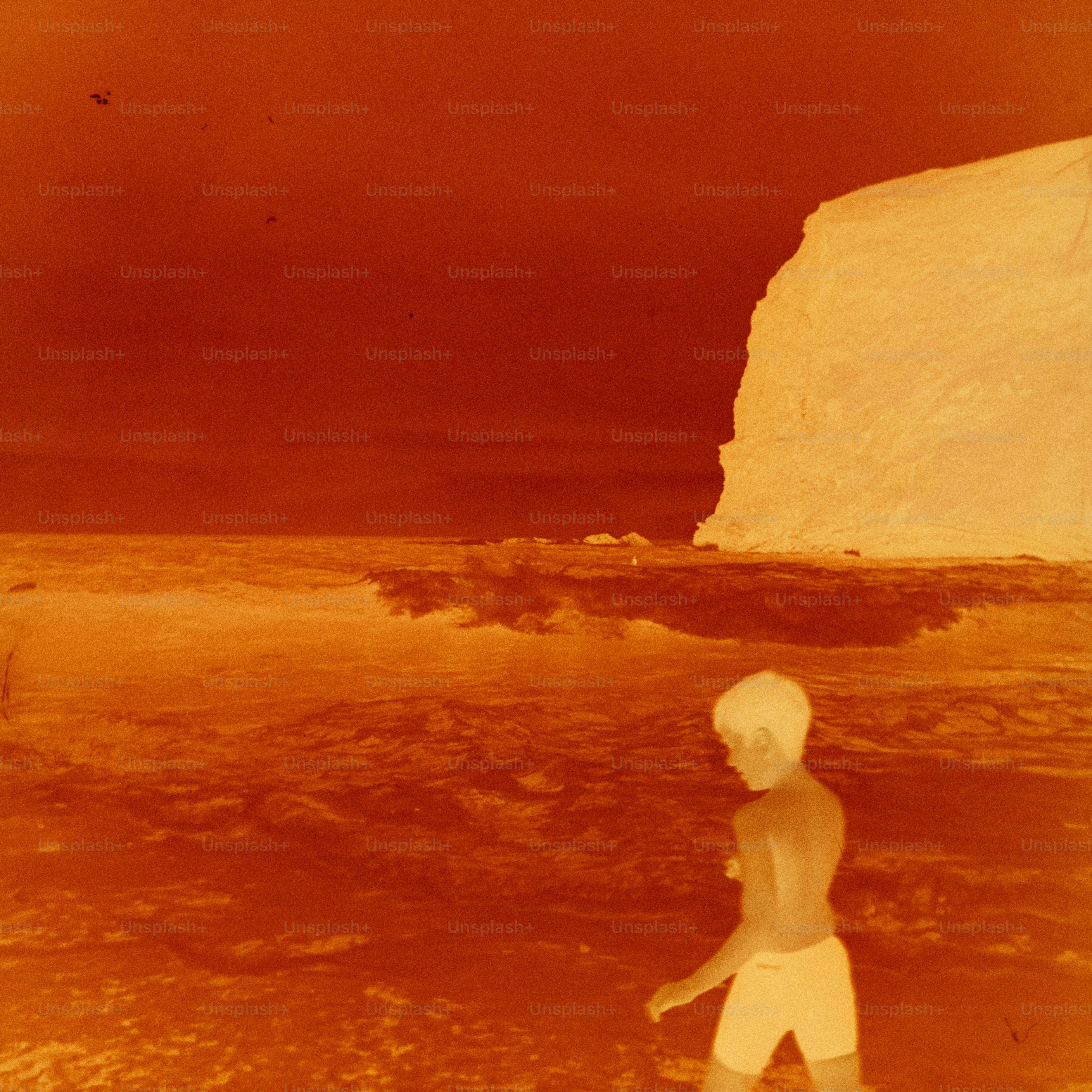 Young person walks along a beach near cliff.