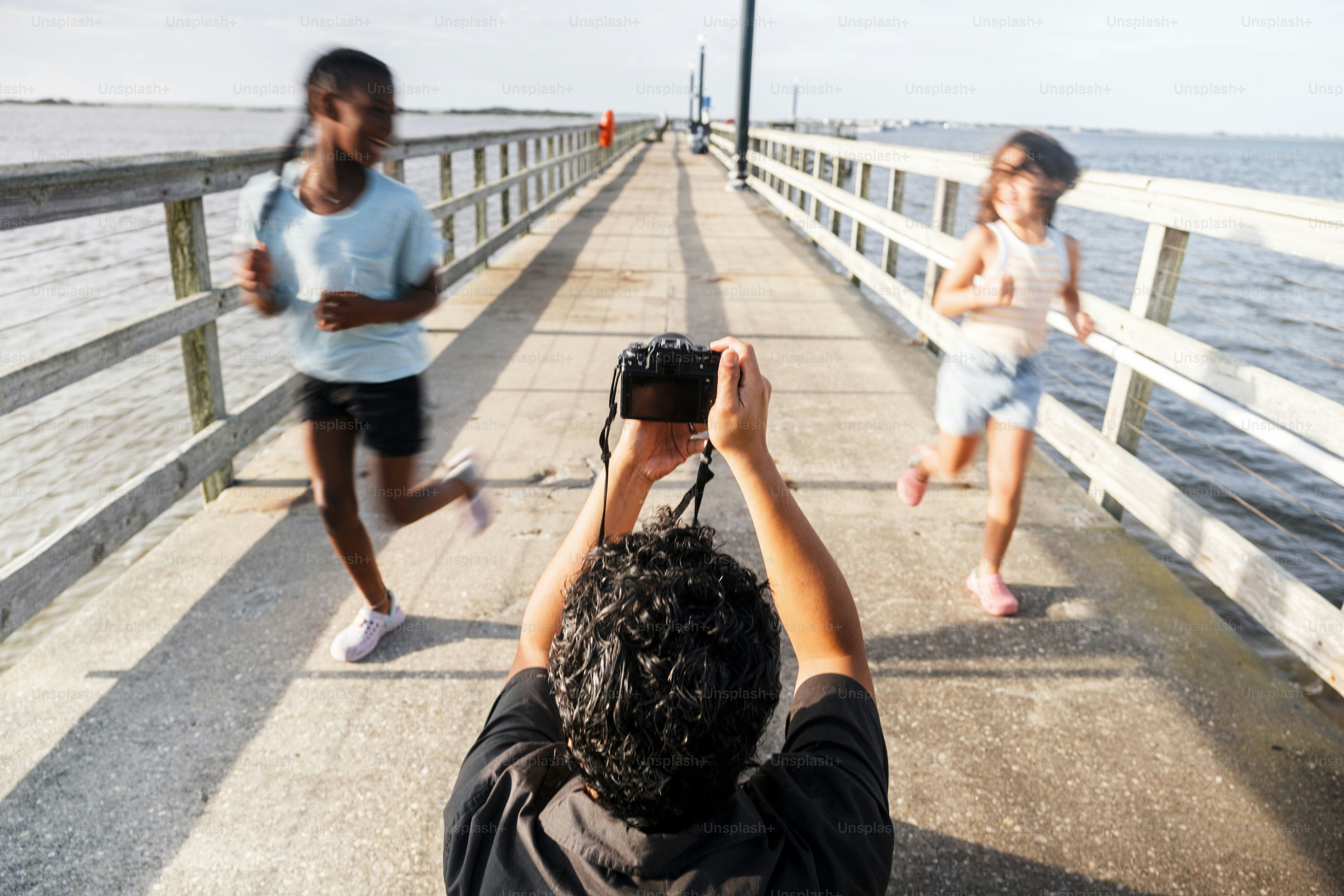 Person photographs two girls running on a pier.