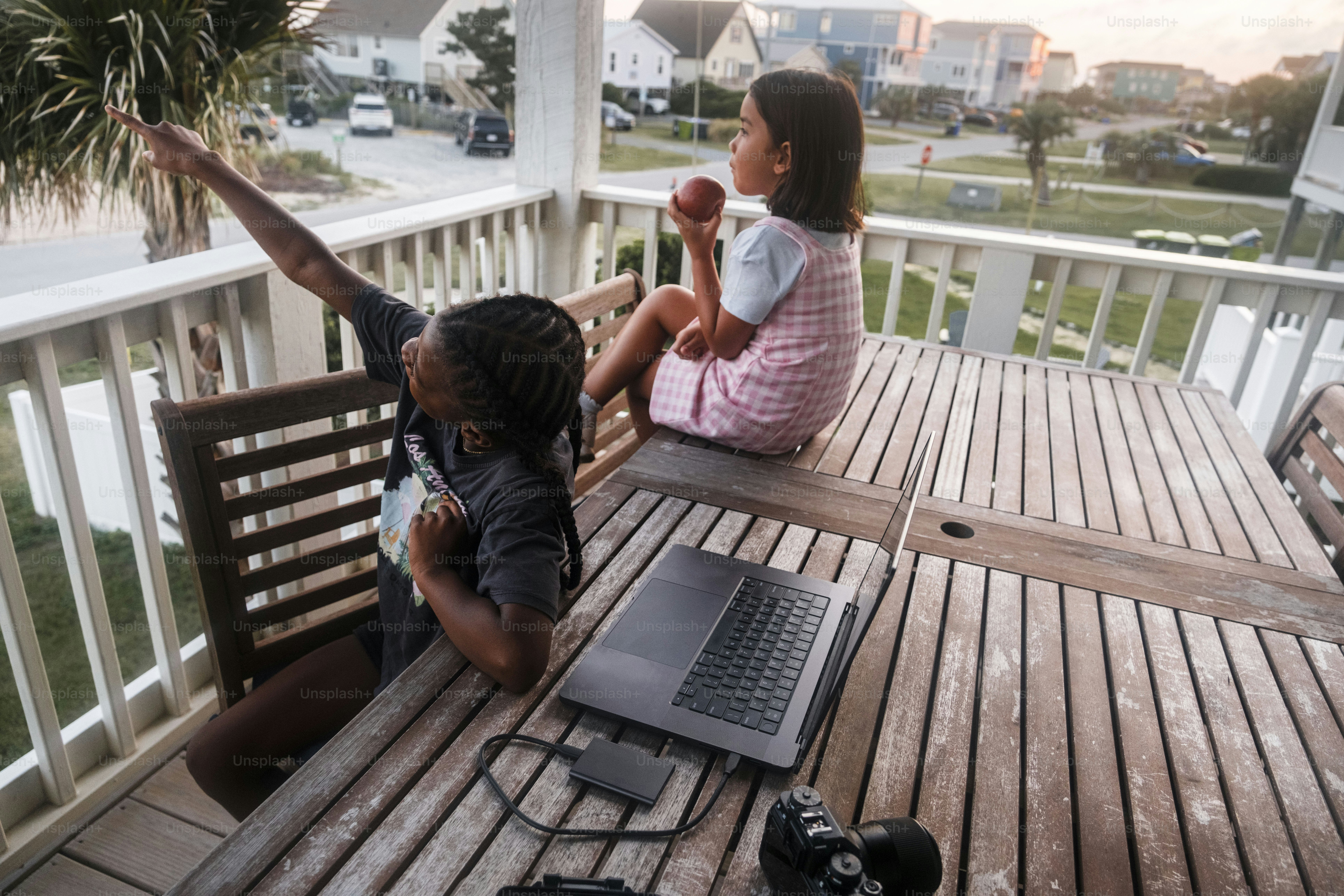 Two girls on a porch with a laptop and snacks.