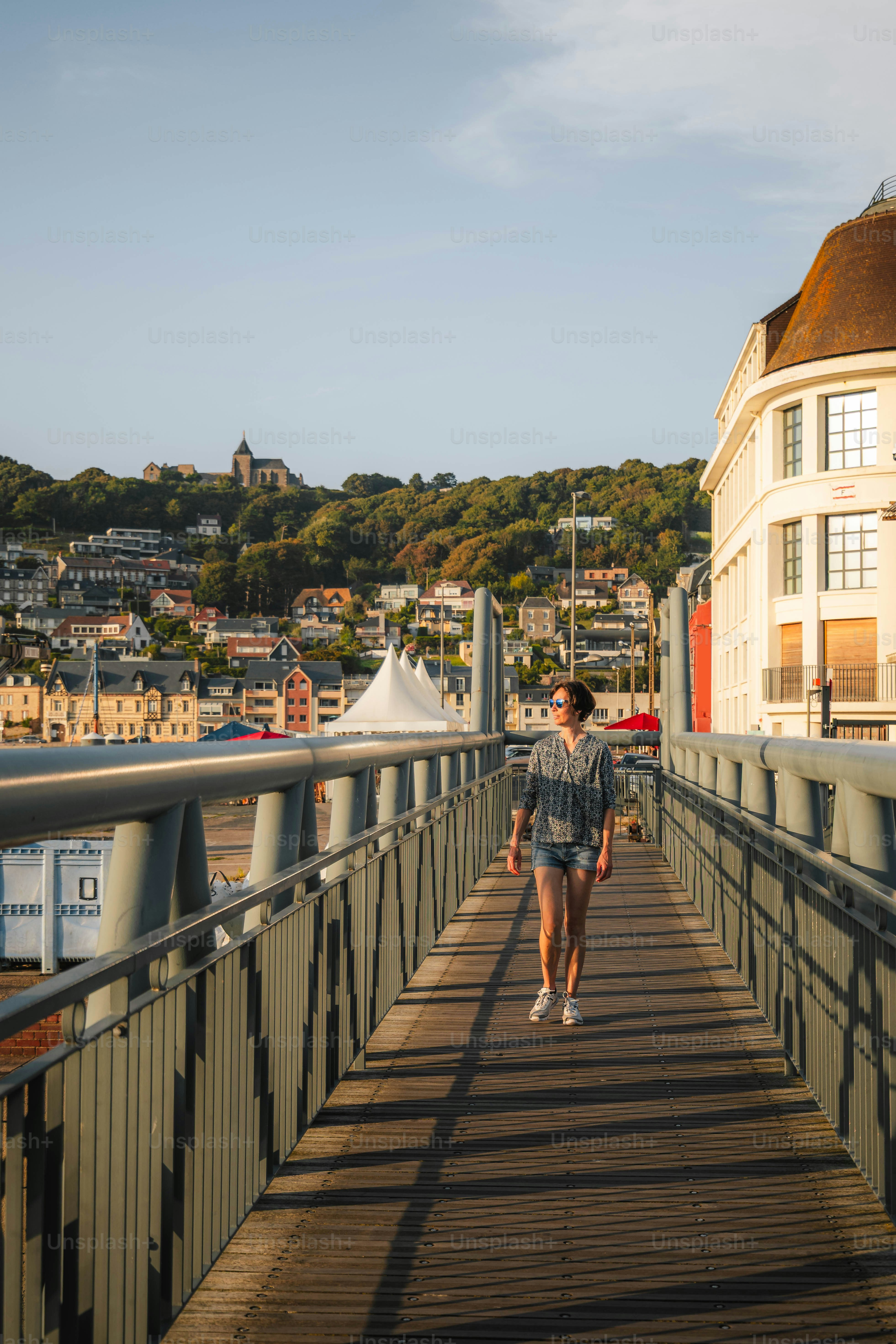 Woman walks on a bridge towards a coastal town.