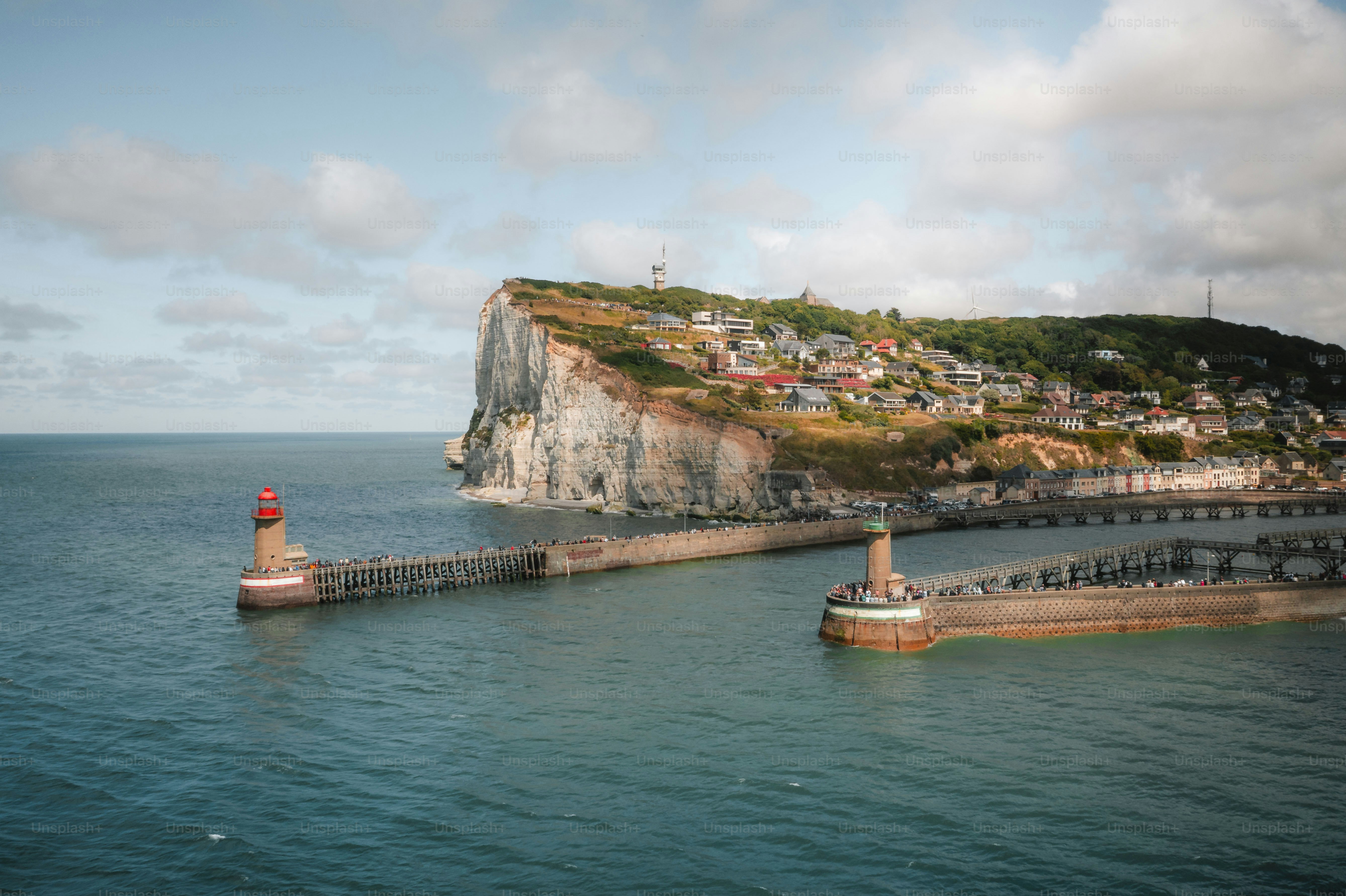 Two lighthouses guard a harbor entrance near a cliffside village.