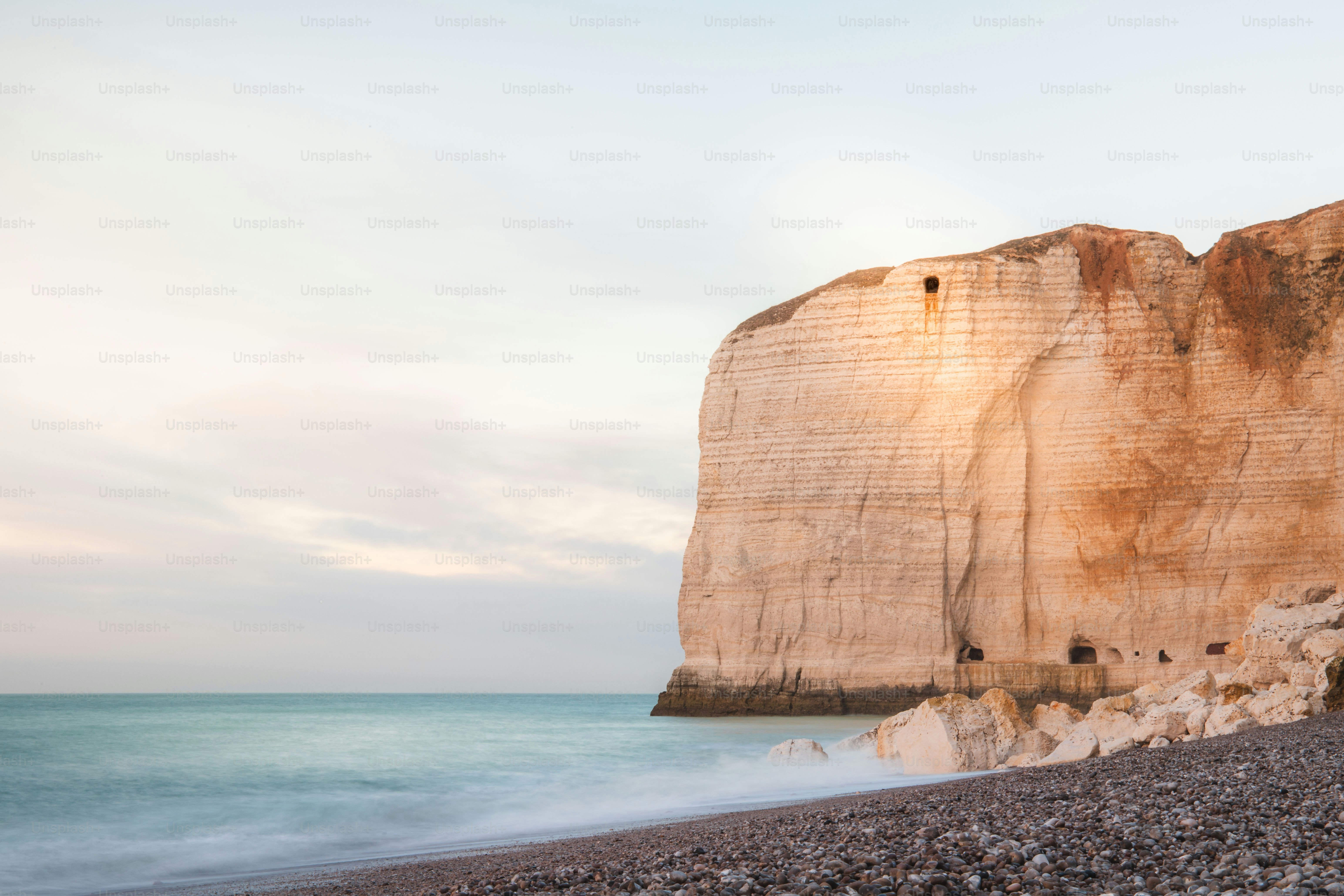 Rocky beach with a large cliff and ocean waves.