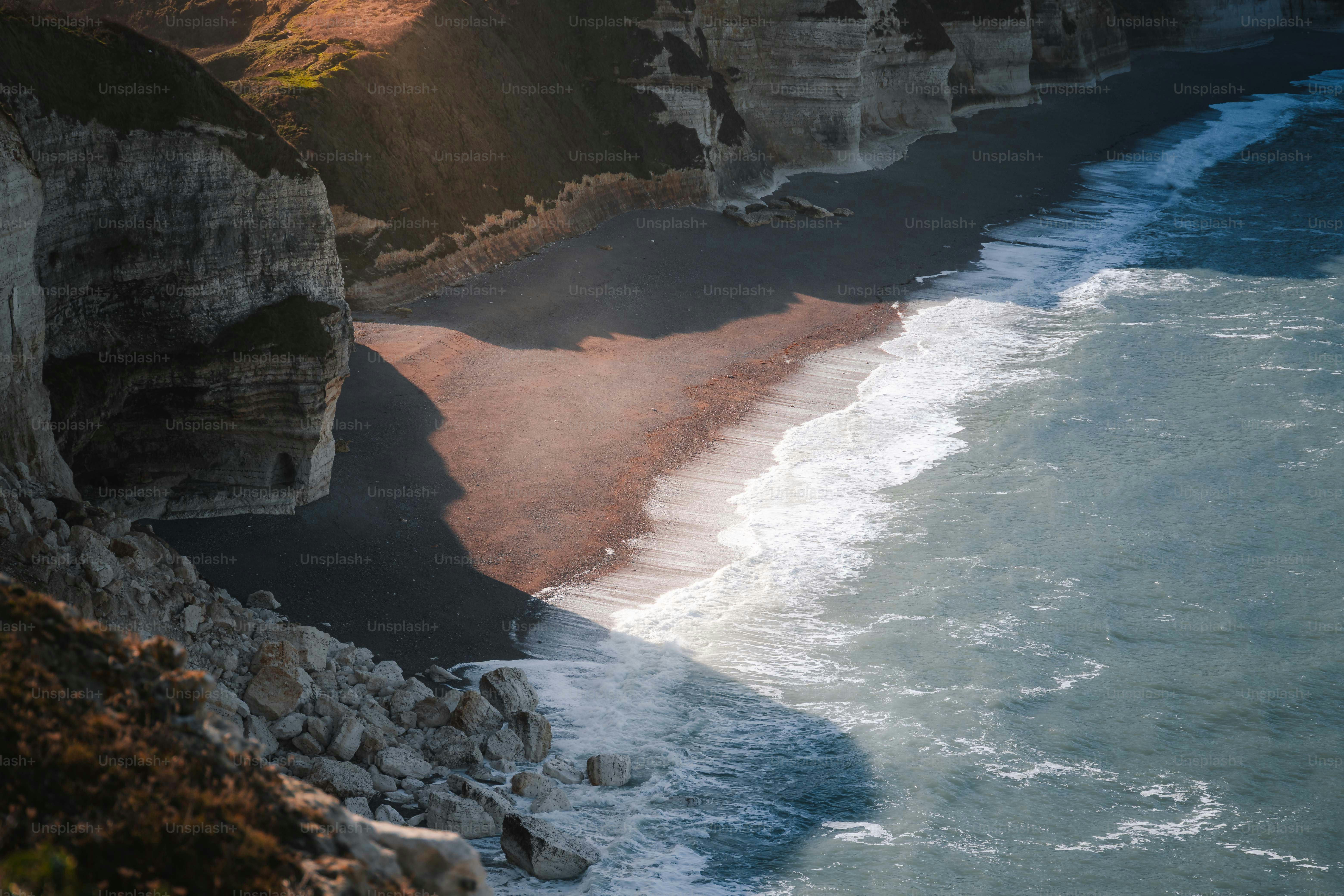 Waves crash on a secluded beach below cliffs.