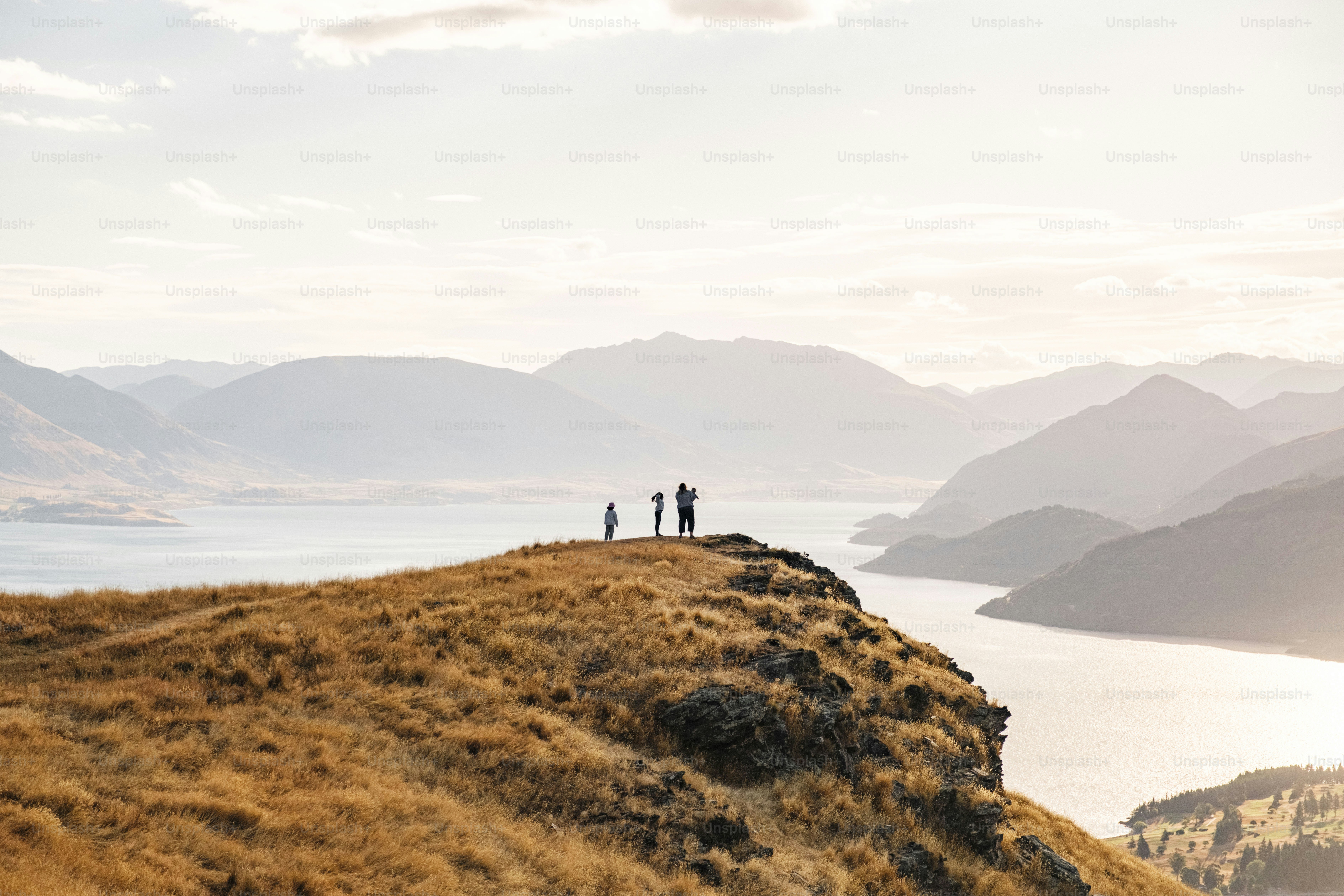 People stand on a grassy cliff overlooking a lake and mountains.