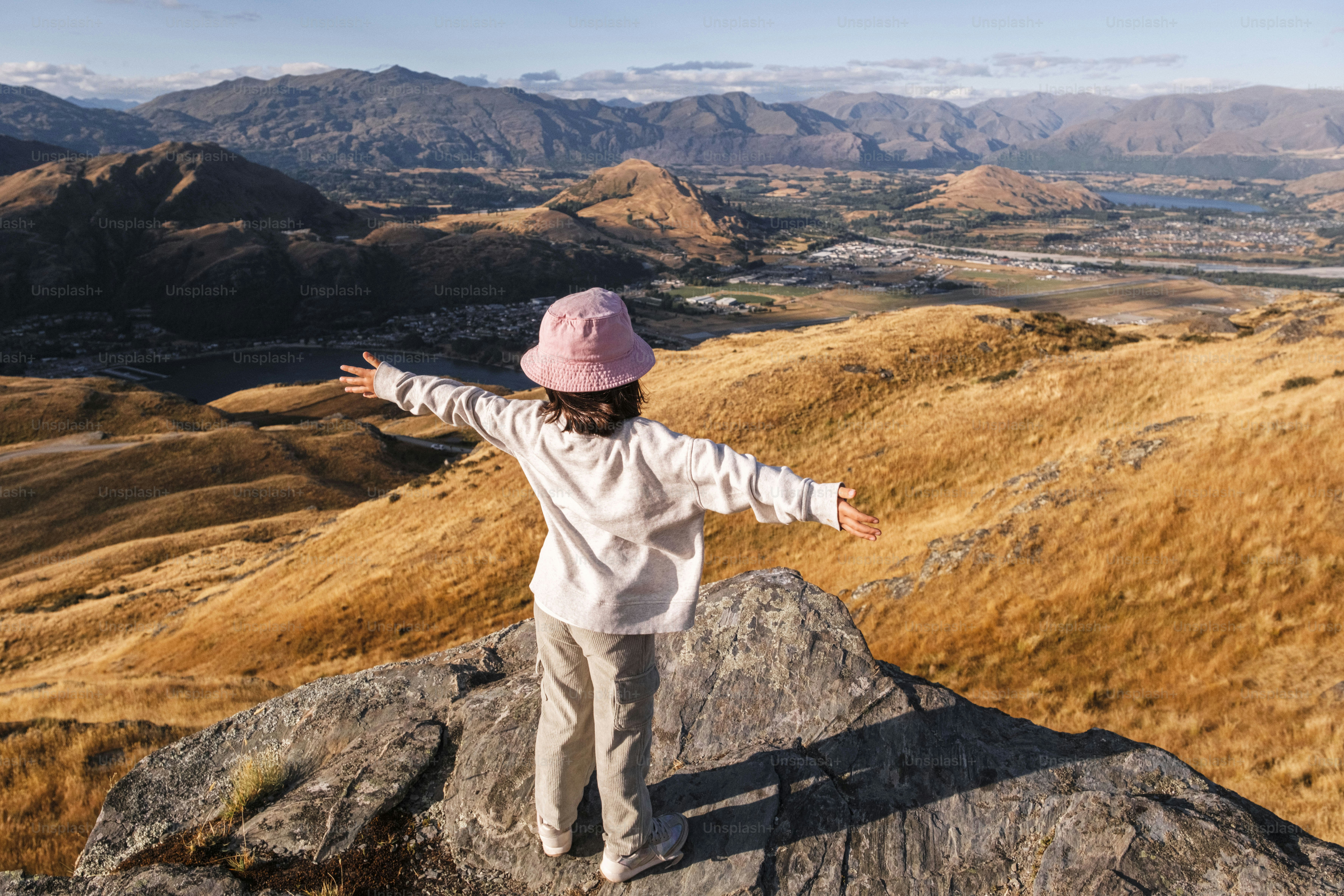 Child with arms outstretched on mountain peak overlooking valley.