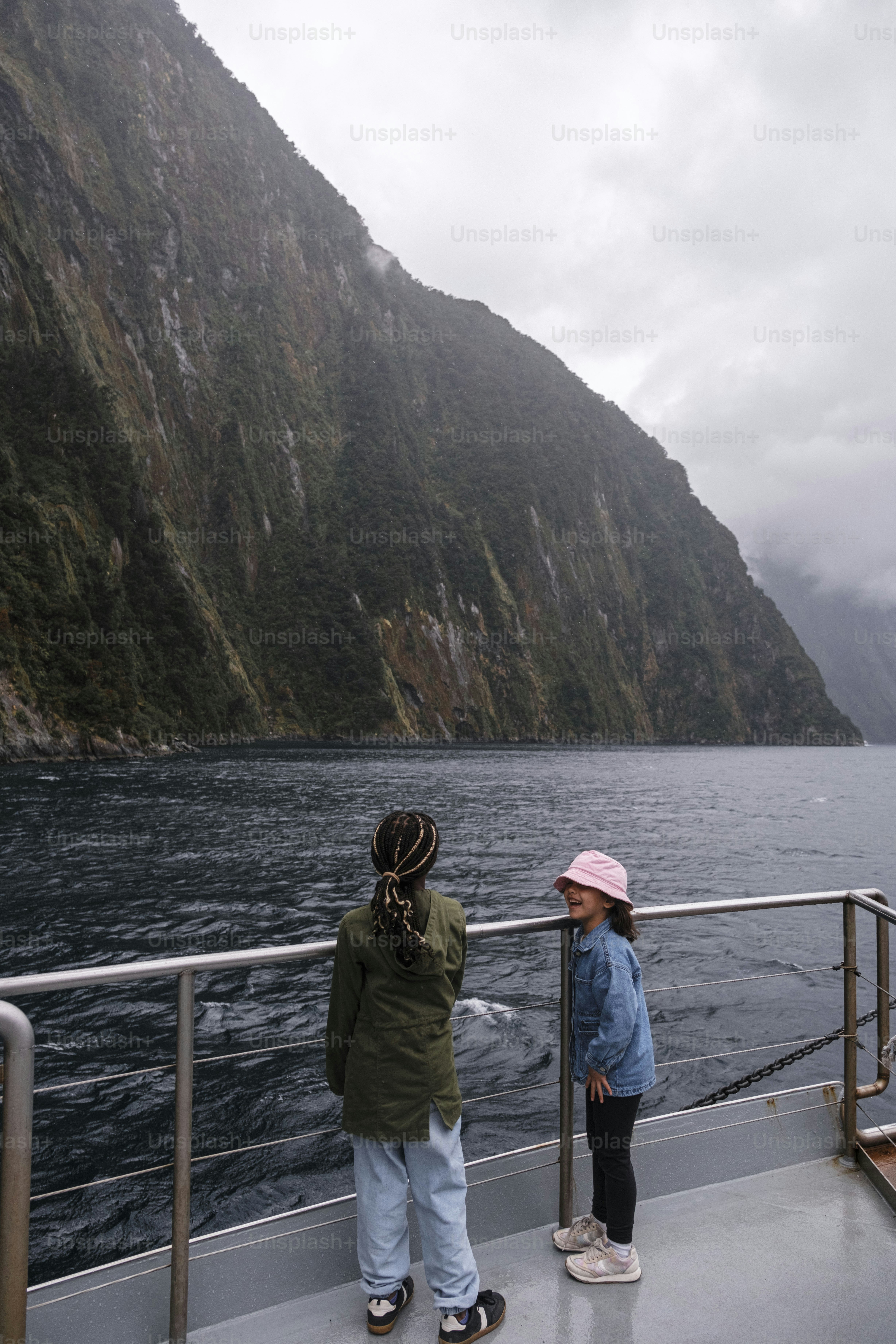 Two girls admire a majestic mountain view from a boat.