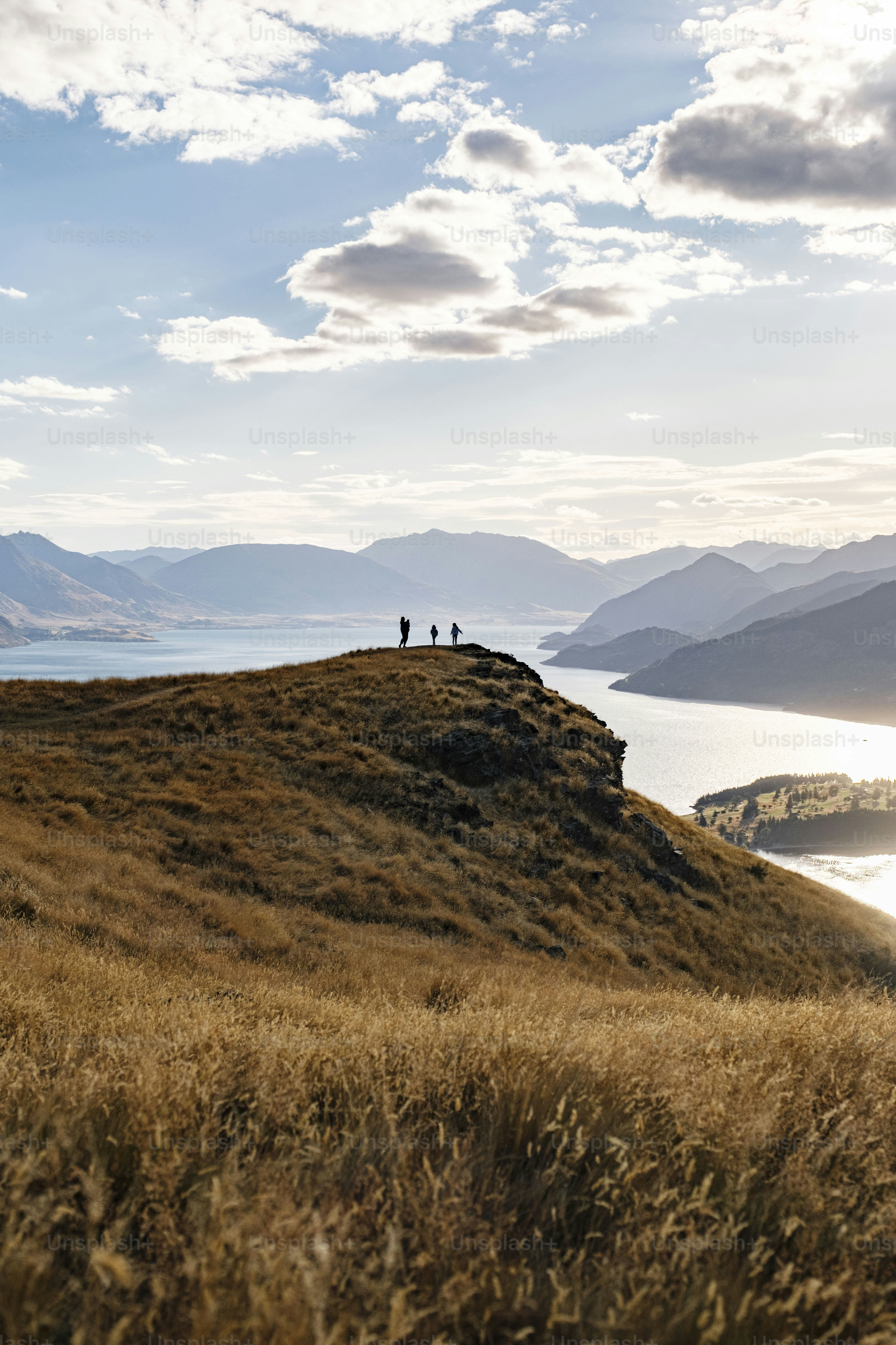 Hikers on a grassy ridge overlooking a vast lake.