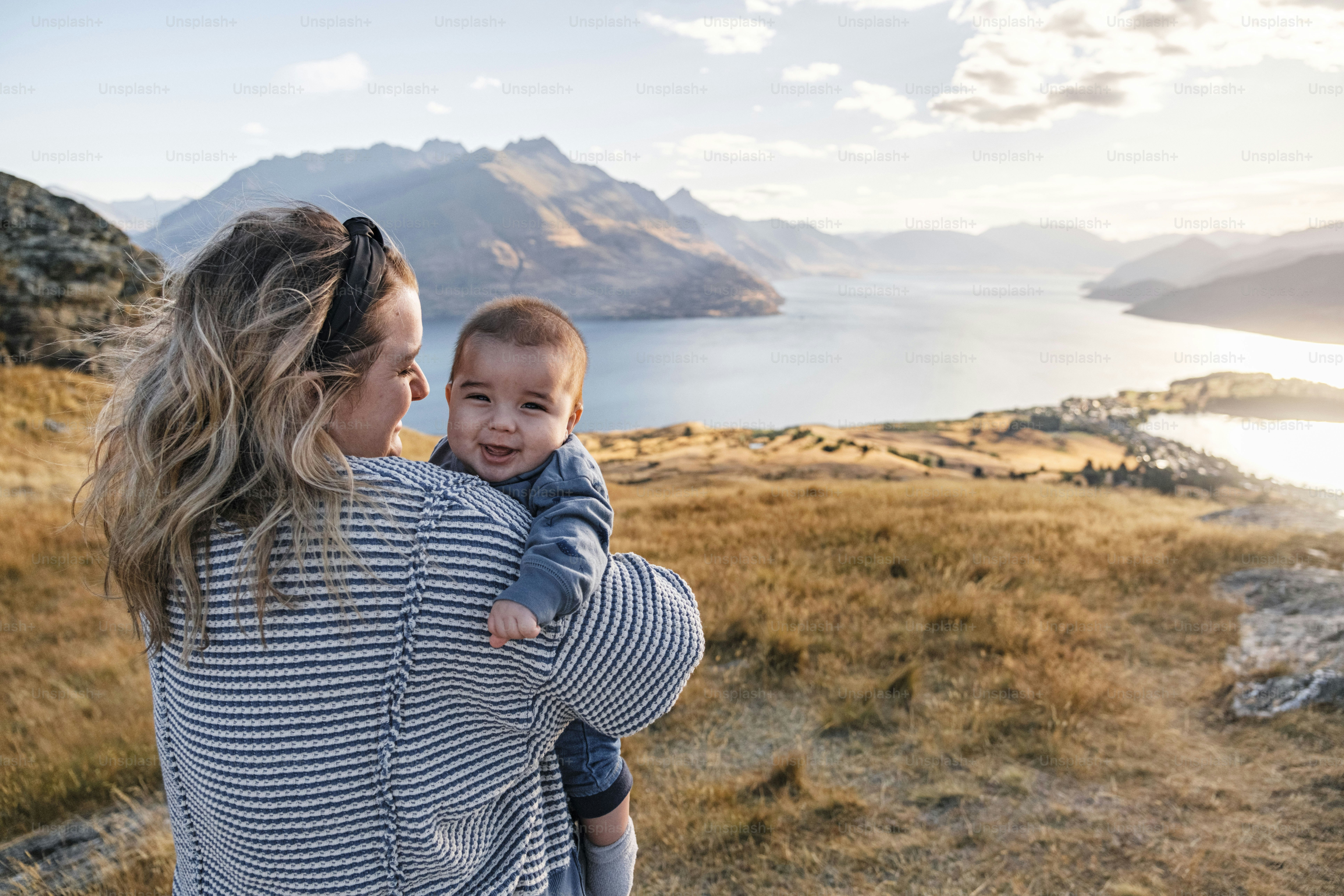 Mother holding smiling baby overlooking scenic lake and mountains