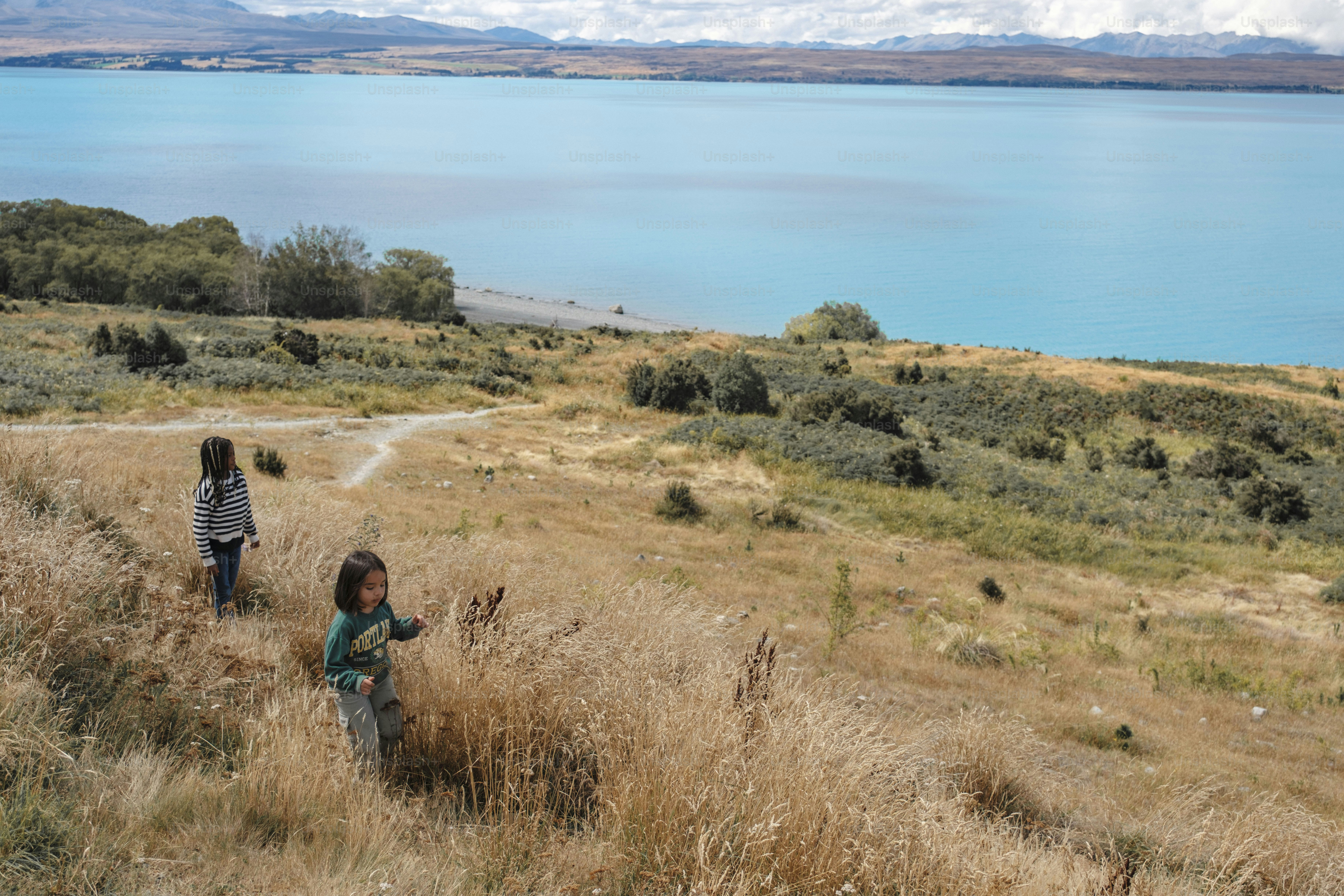 Dos niños caminan por la hierba seca cerca de un lago.