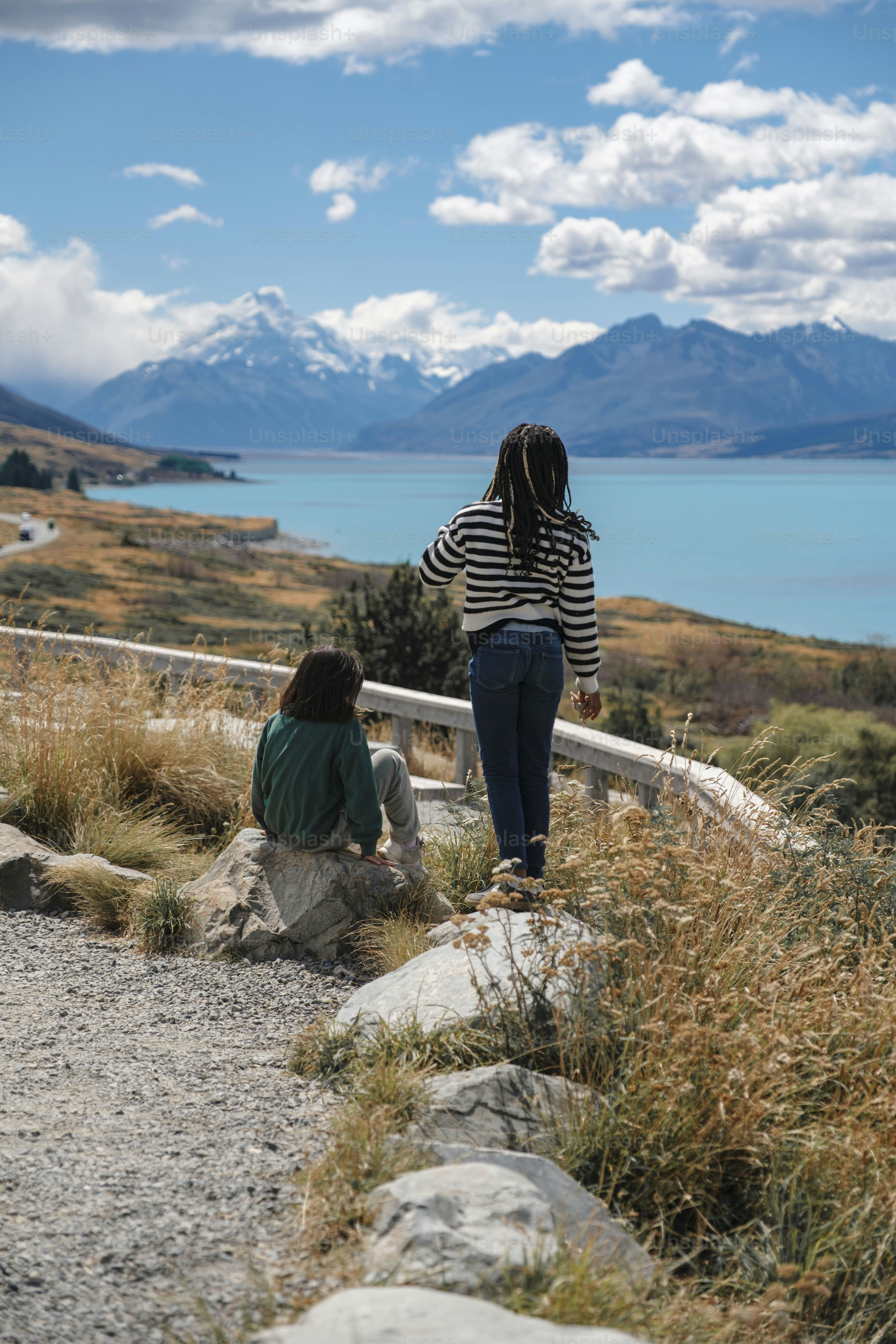 Dos personas admiran un lago turquesa y montañas nevadas.