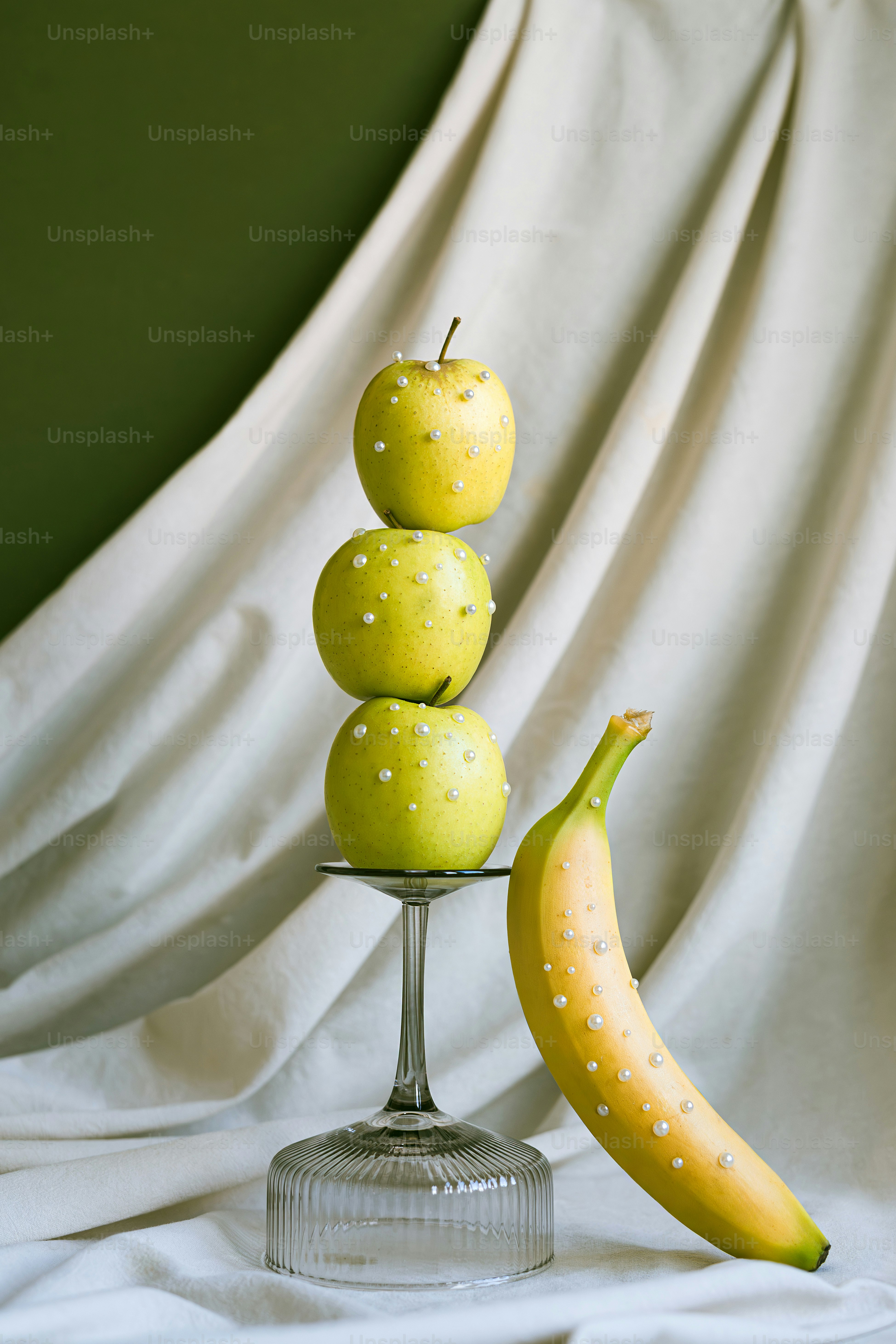 Tres manzanas apiladas en un soporte de vidrio con plátano