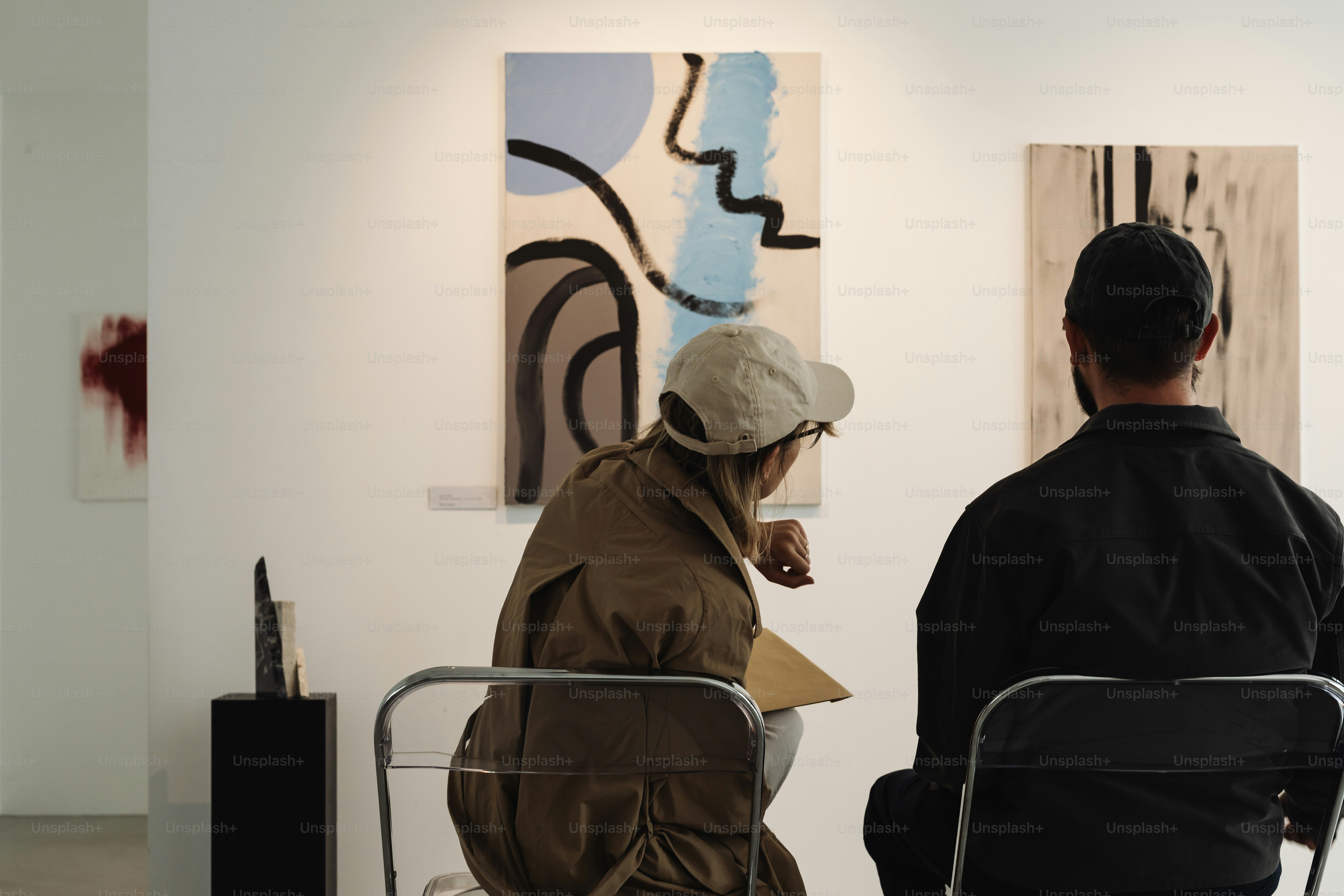 Two people observe abstract paintings in a gallery.