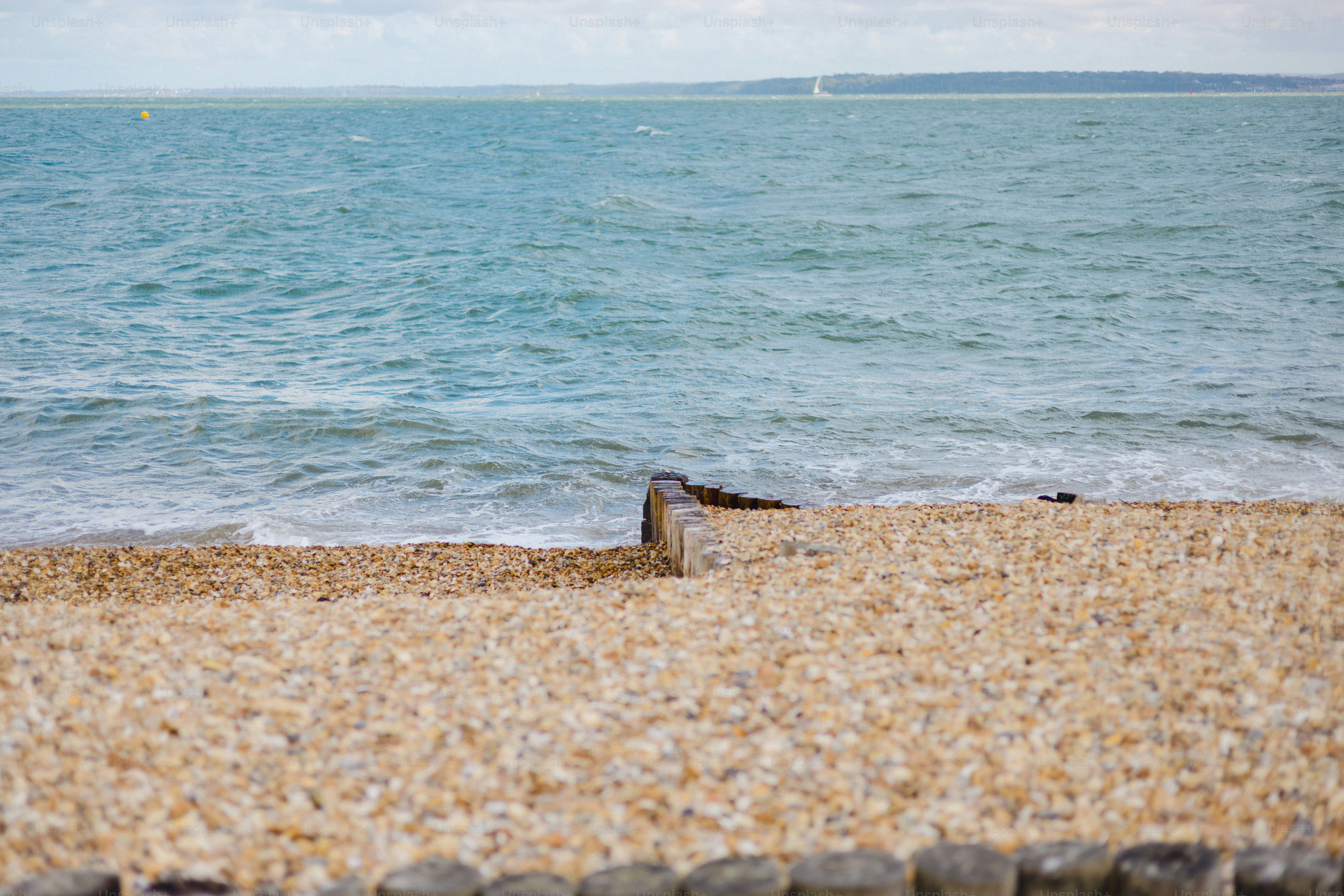 Pebble beach with calm ocean waves and wooden posts.