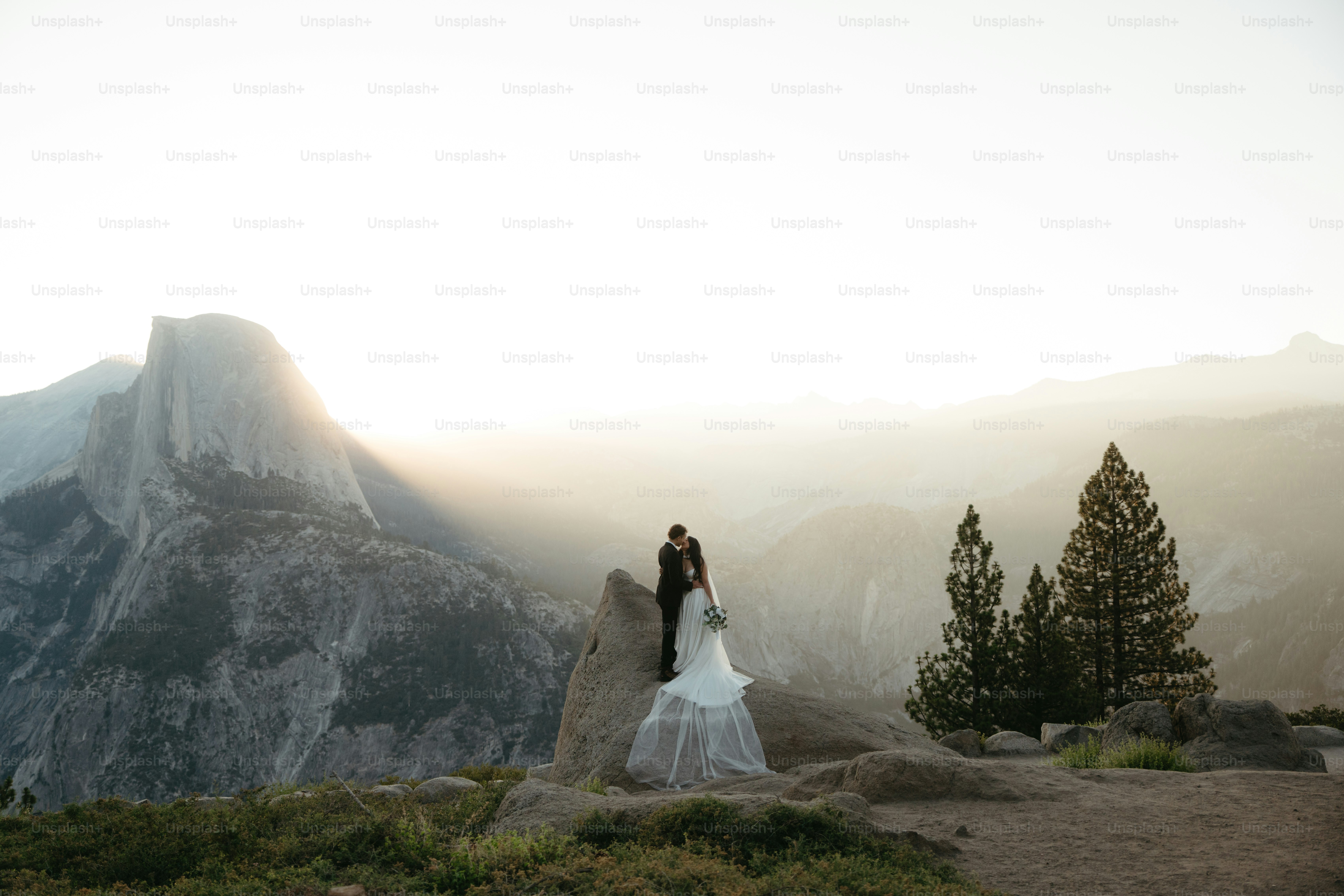 Newlyweds embrace on a rock with mountain backdrop