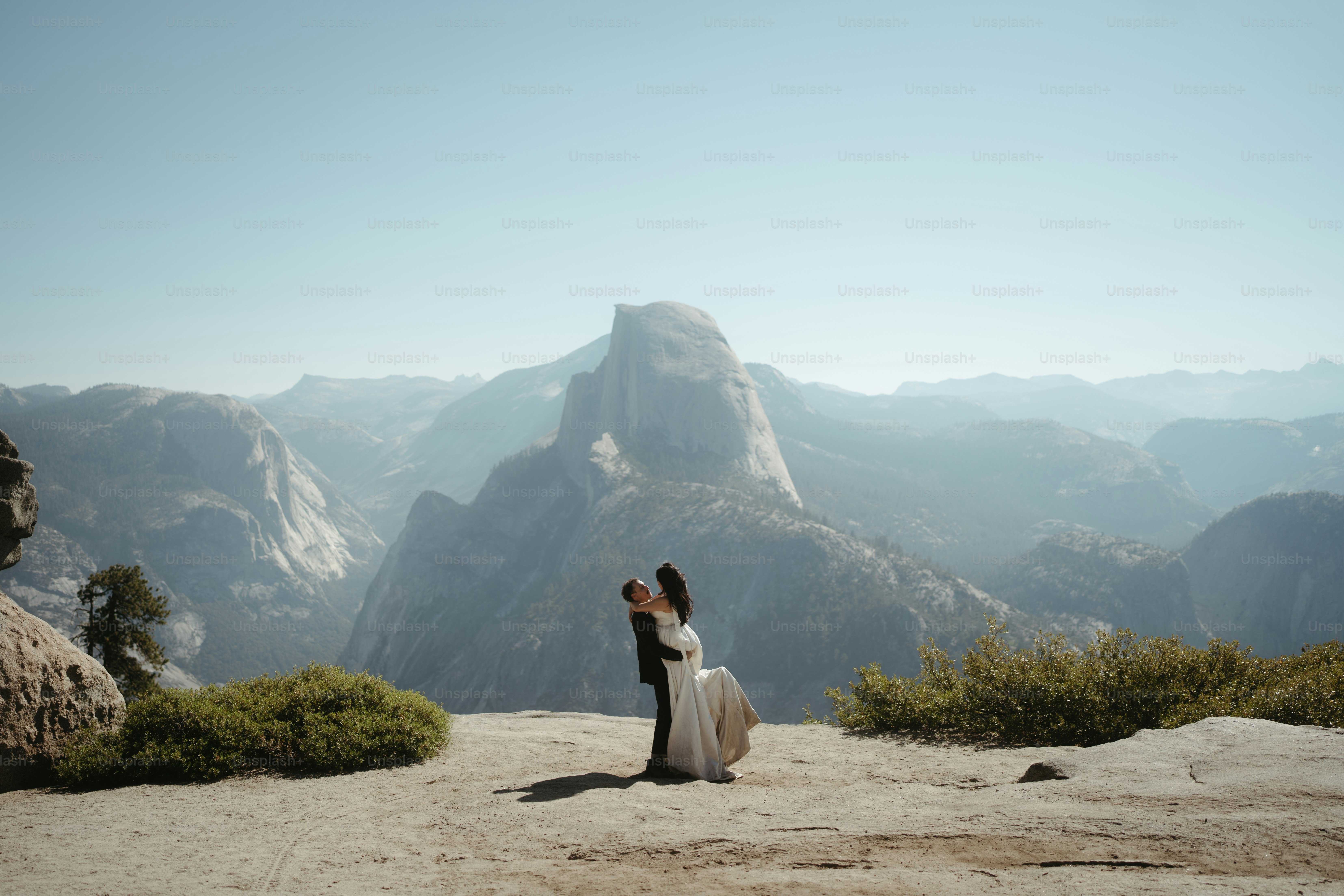 Couple embracing on cliff with mountain backdrop