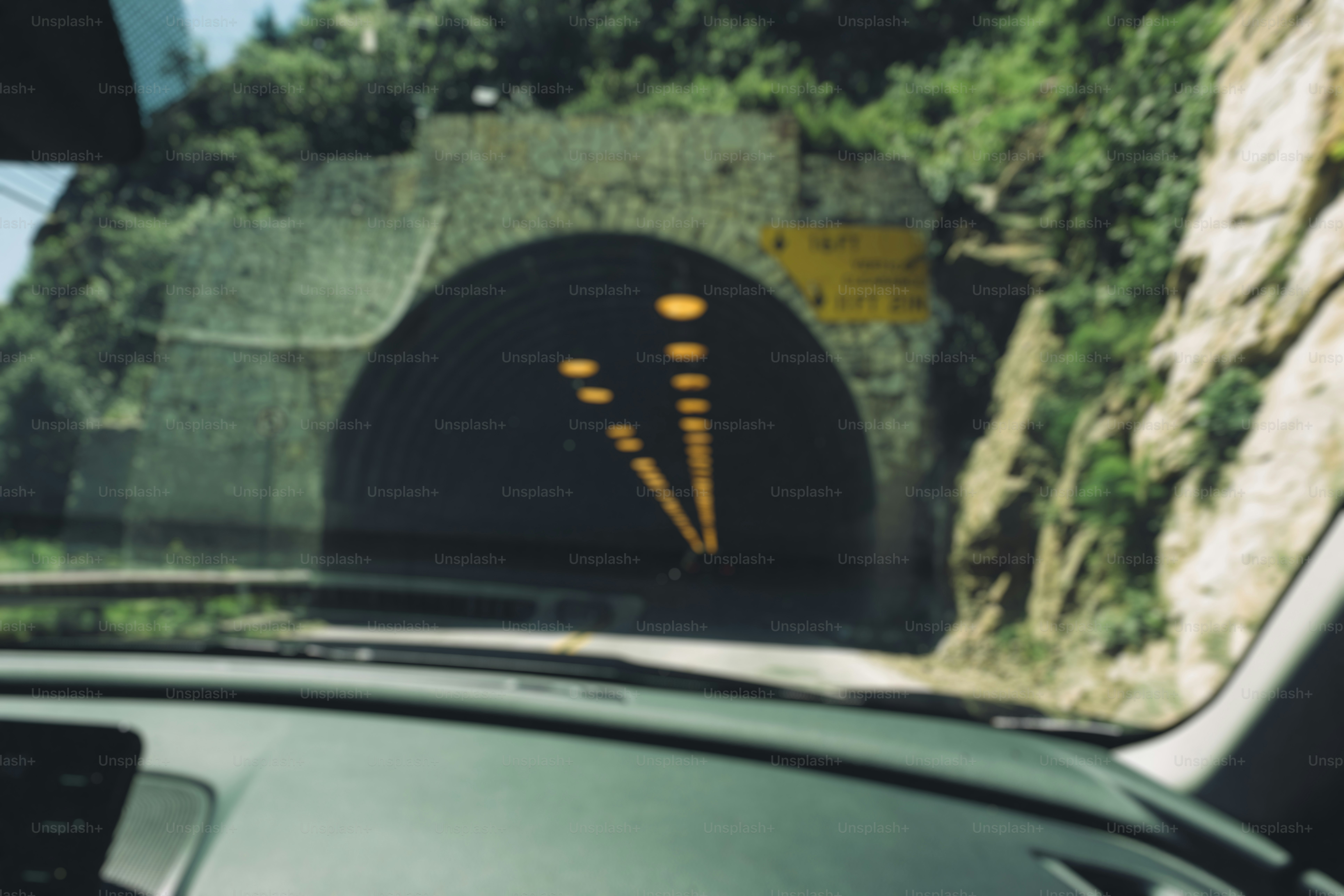 View from car entering a stone tunnel with lights.