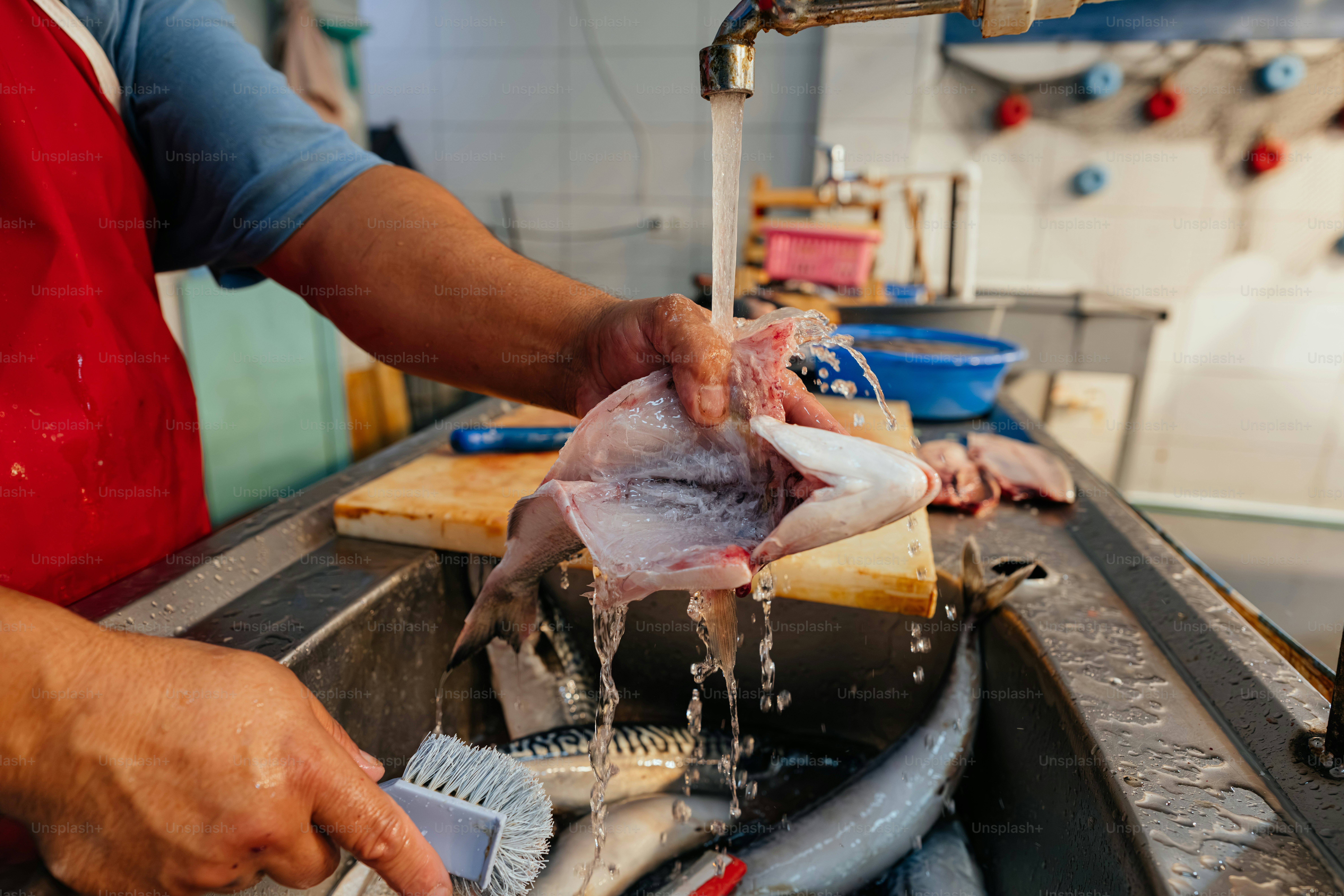 A person washes fish under running water in a sink.