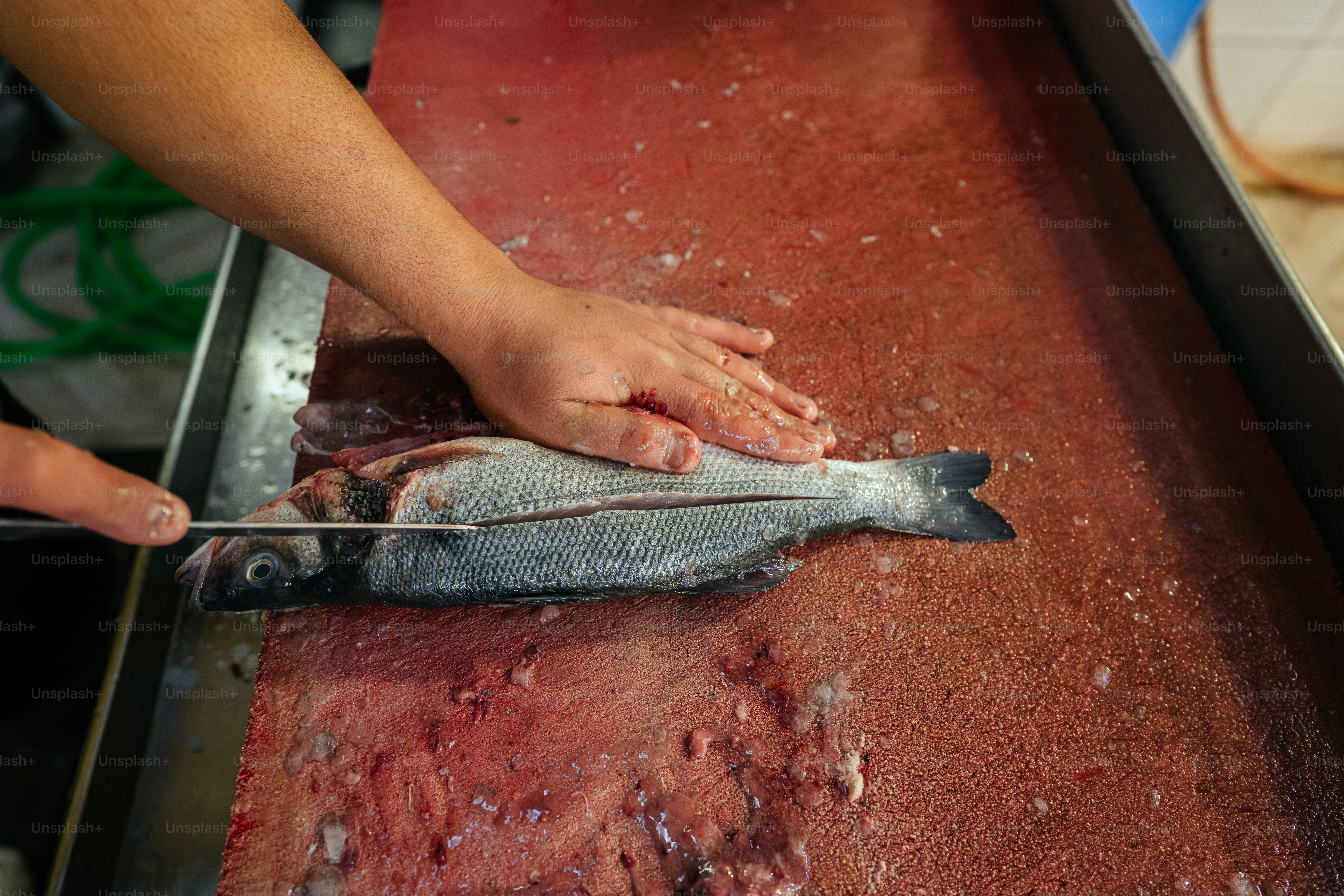 Hands preparing a fish on a red cutting board