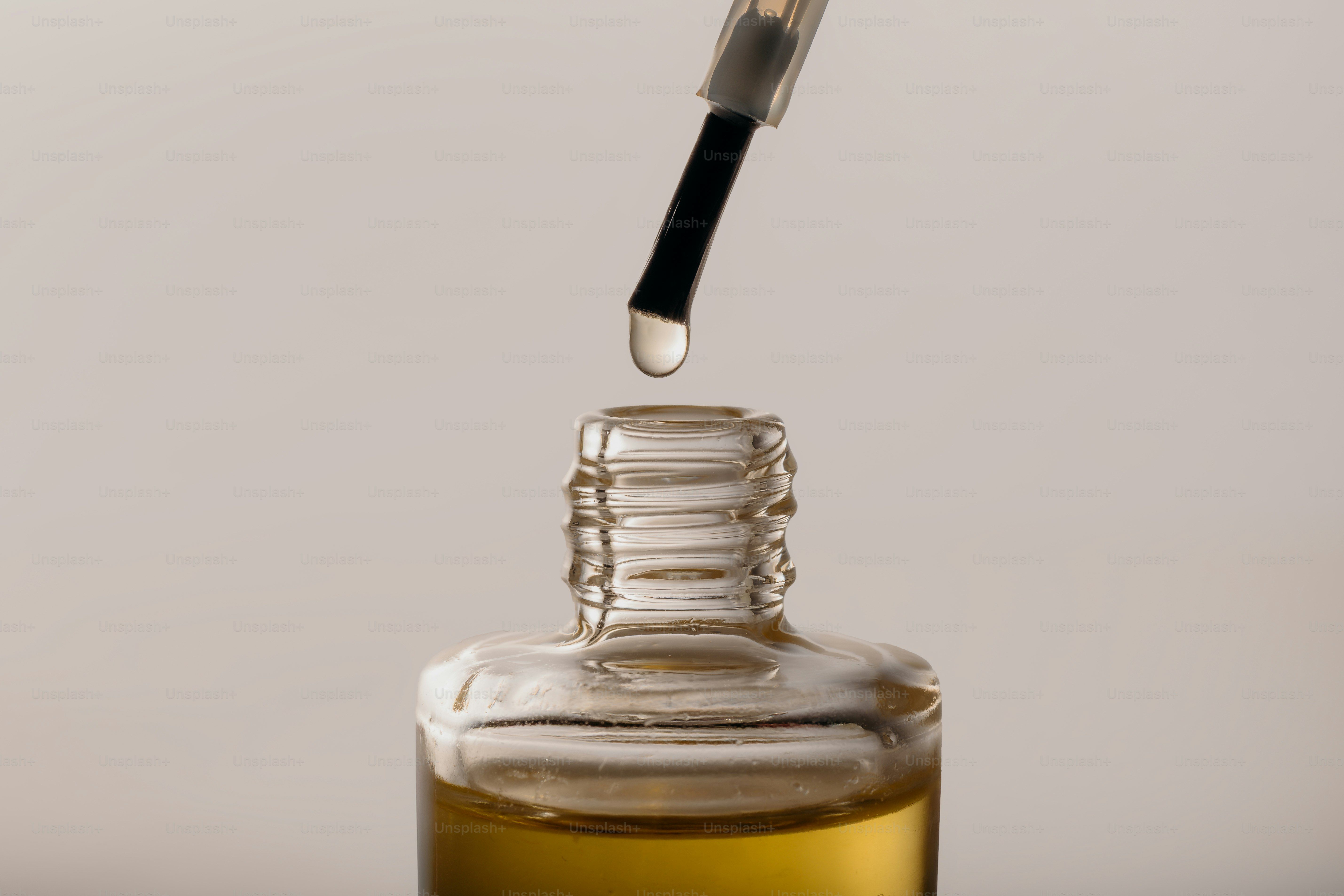 A drop of liquid falls from a brush into a bottle.