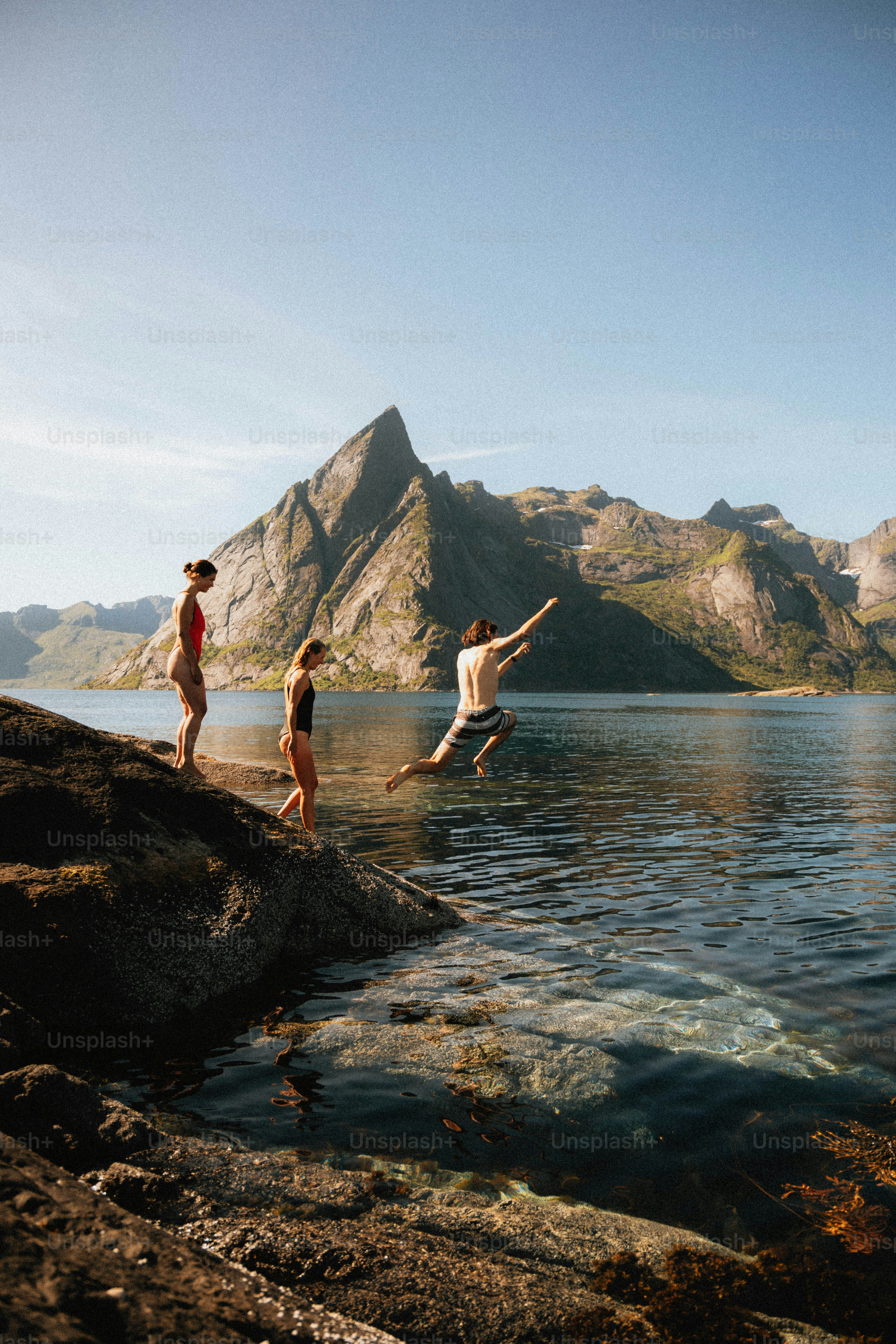 Amigos pulando em águas claras com montanhas atrás