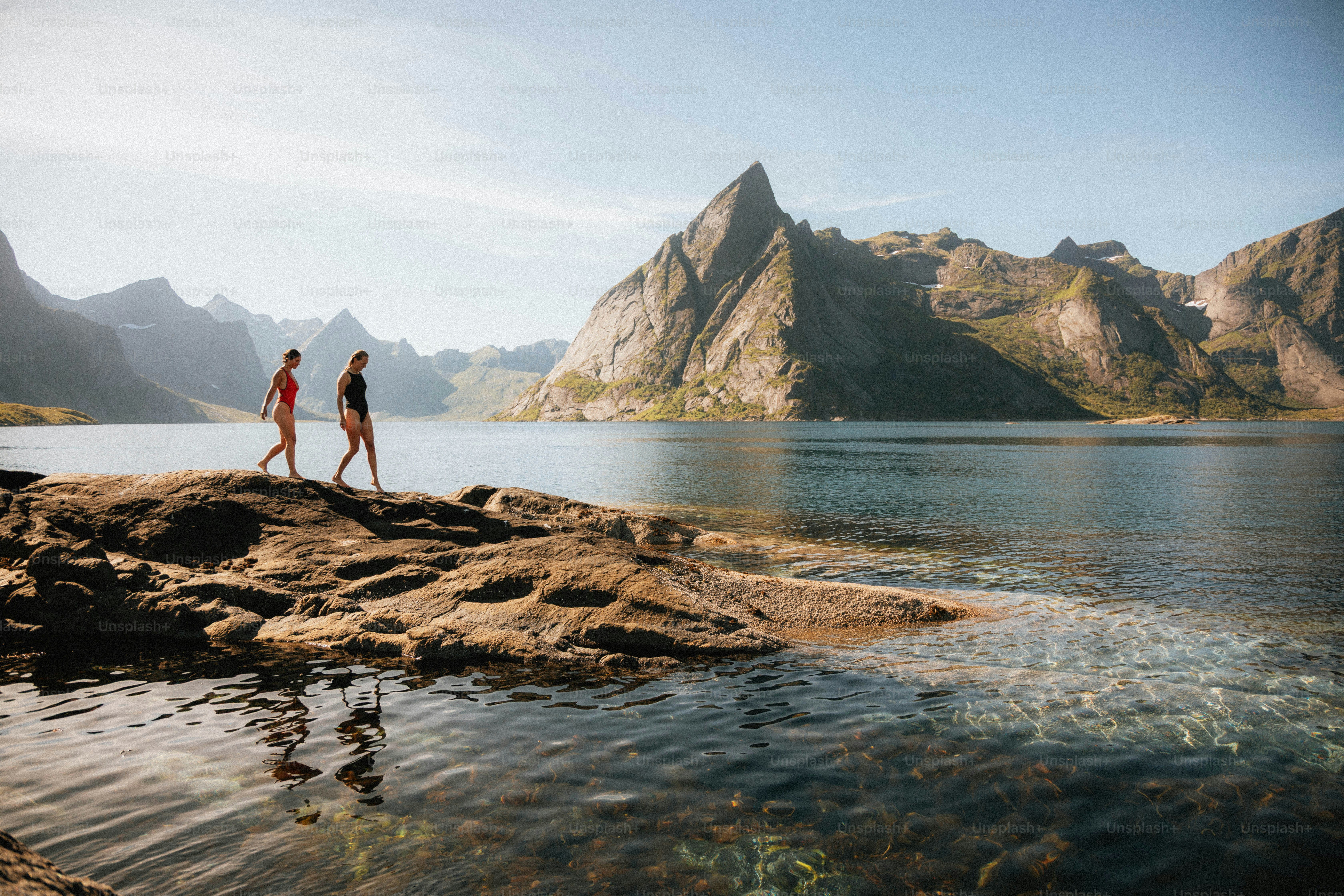 Deux personnes marchent le long d’un rivage rocheux avec des montagnes.