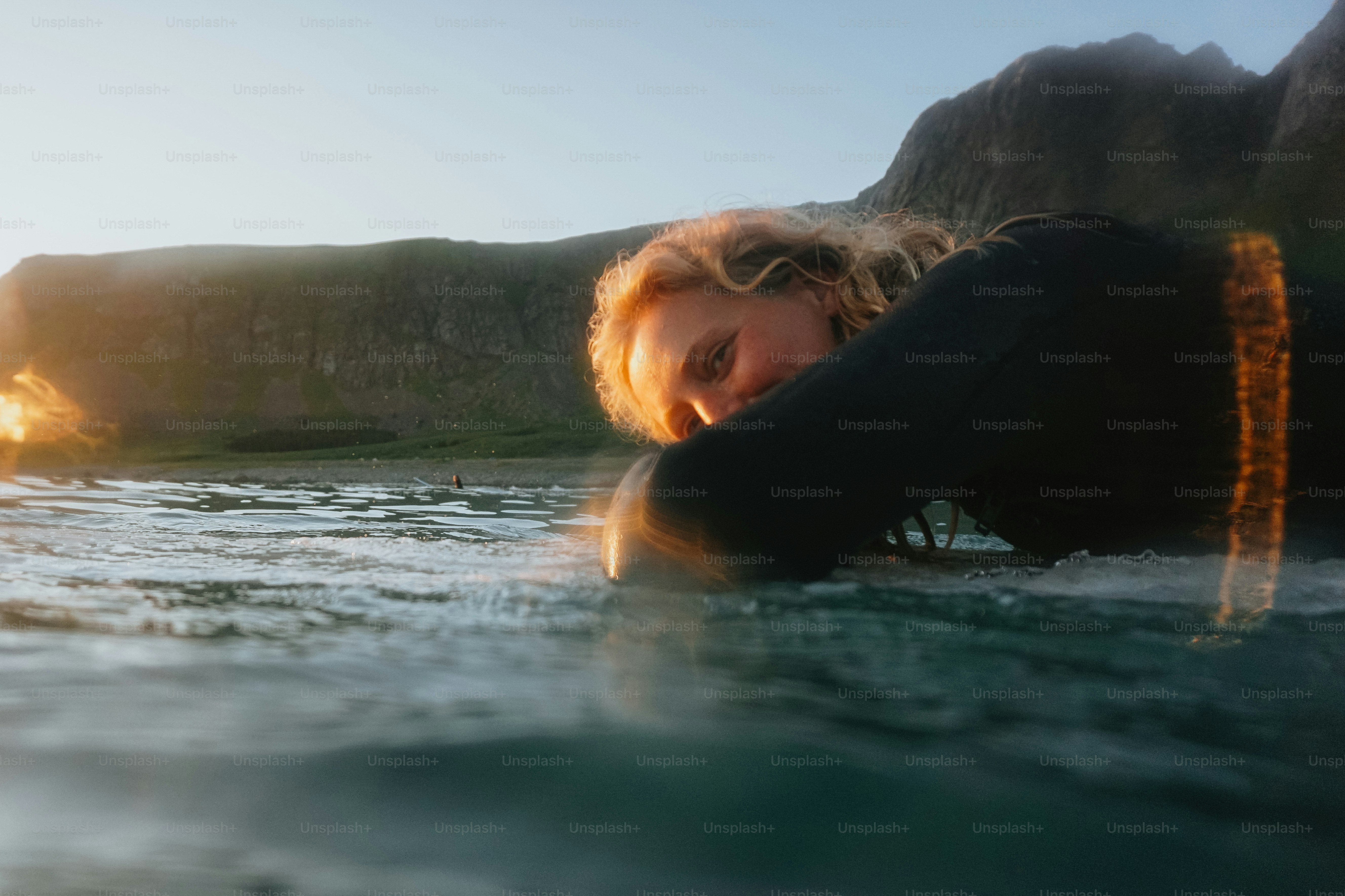 Le surfeur se repose sur une planche de surf au lever du soleil près des montagnes.