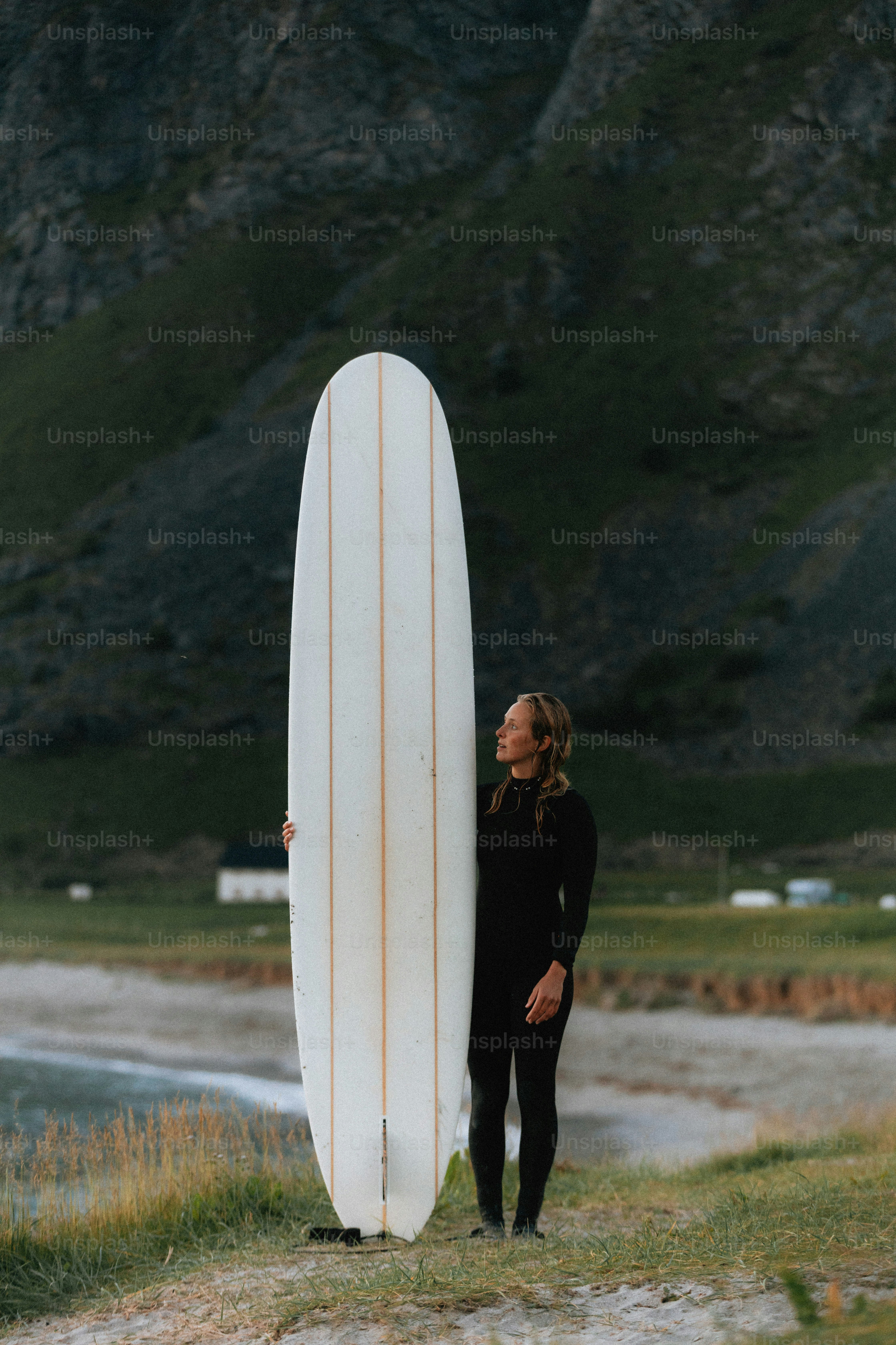 Femme en combinaison de plongée tenant une planche de surf près des montagnes