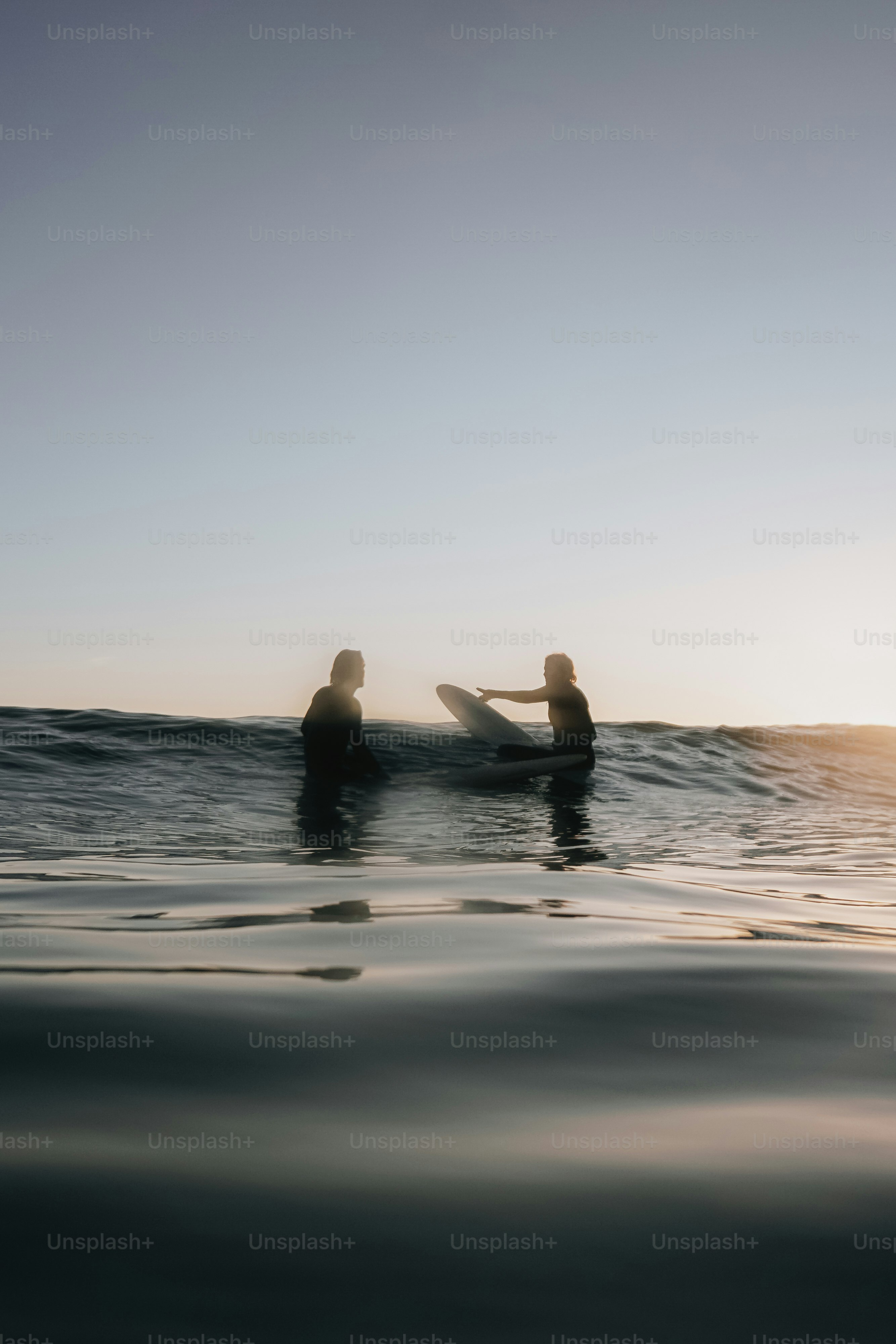 Deux surfeurs pagayant sur un océan calme au coucher du soleil