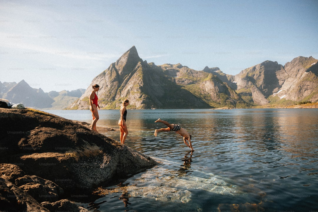 People jumping into clear water near mountains
