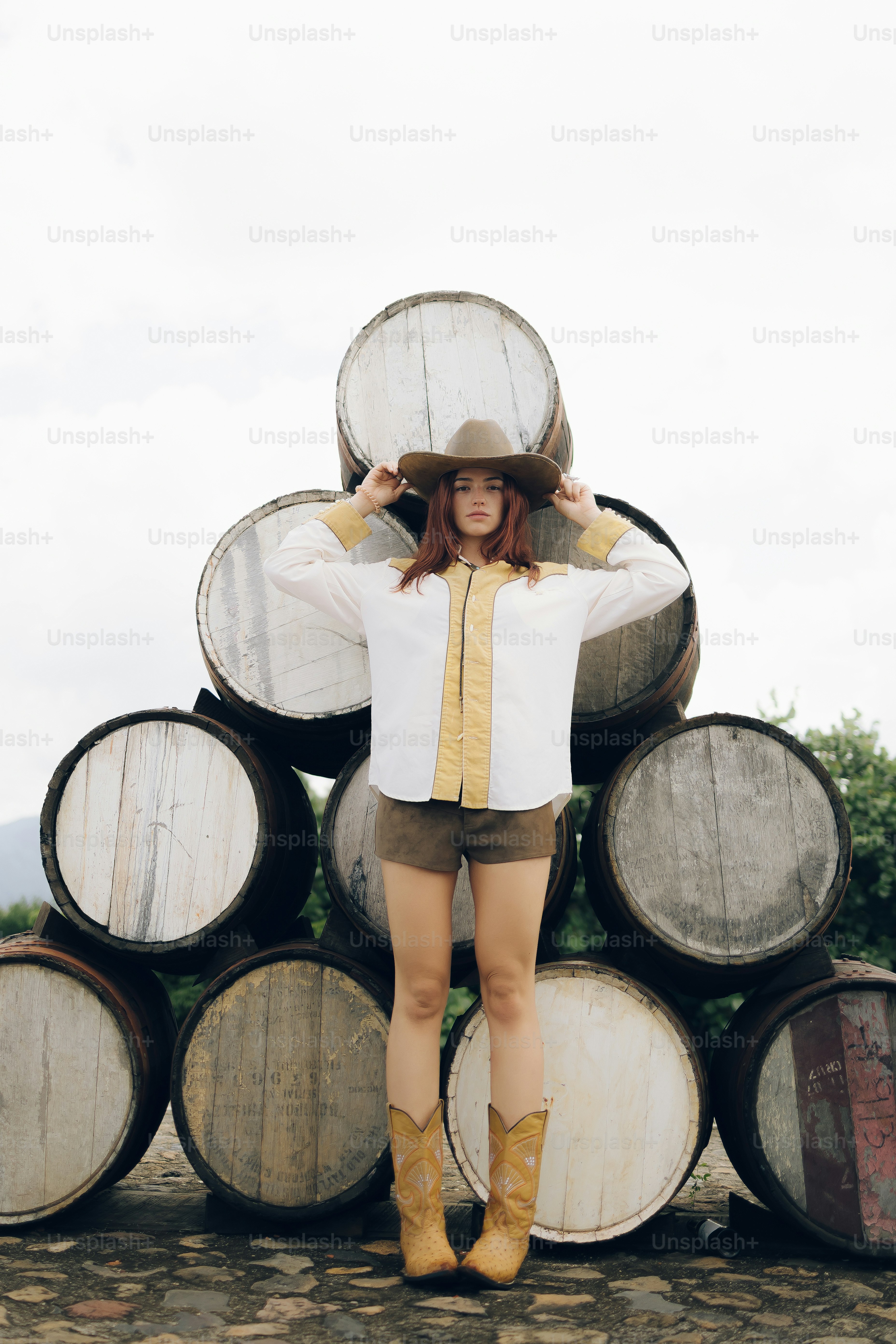Woman in cowboy hat and boots stands by stacked barrels