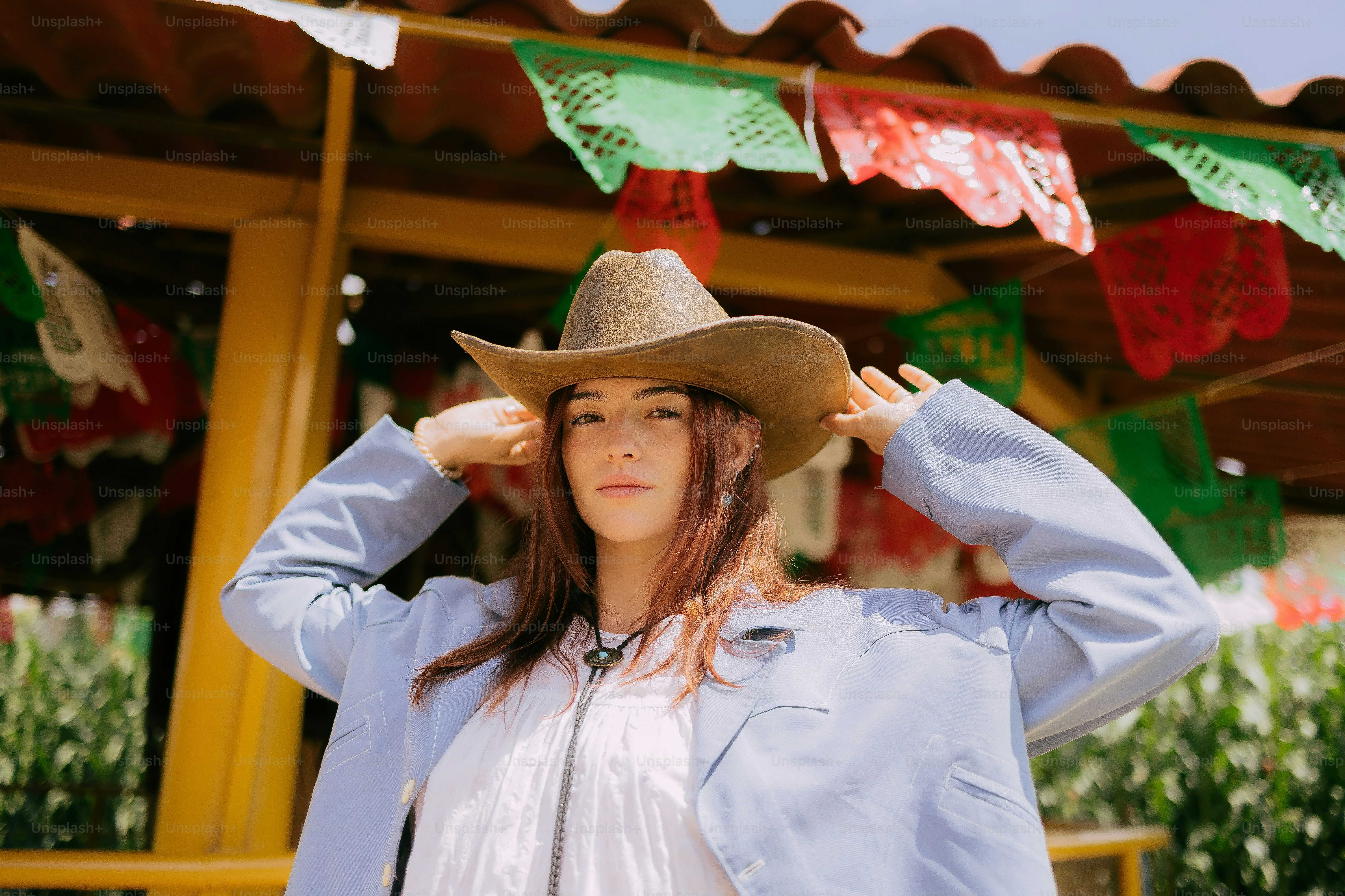 Woman in cowboy hat adjusts hat near colorful decorations