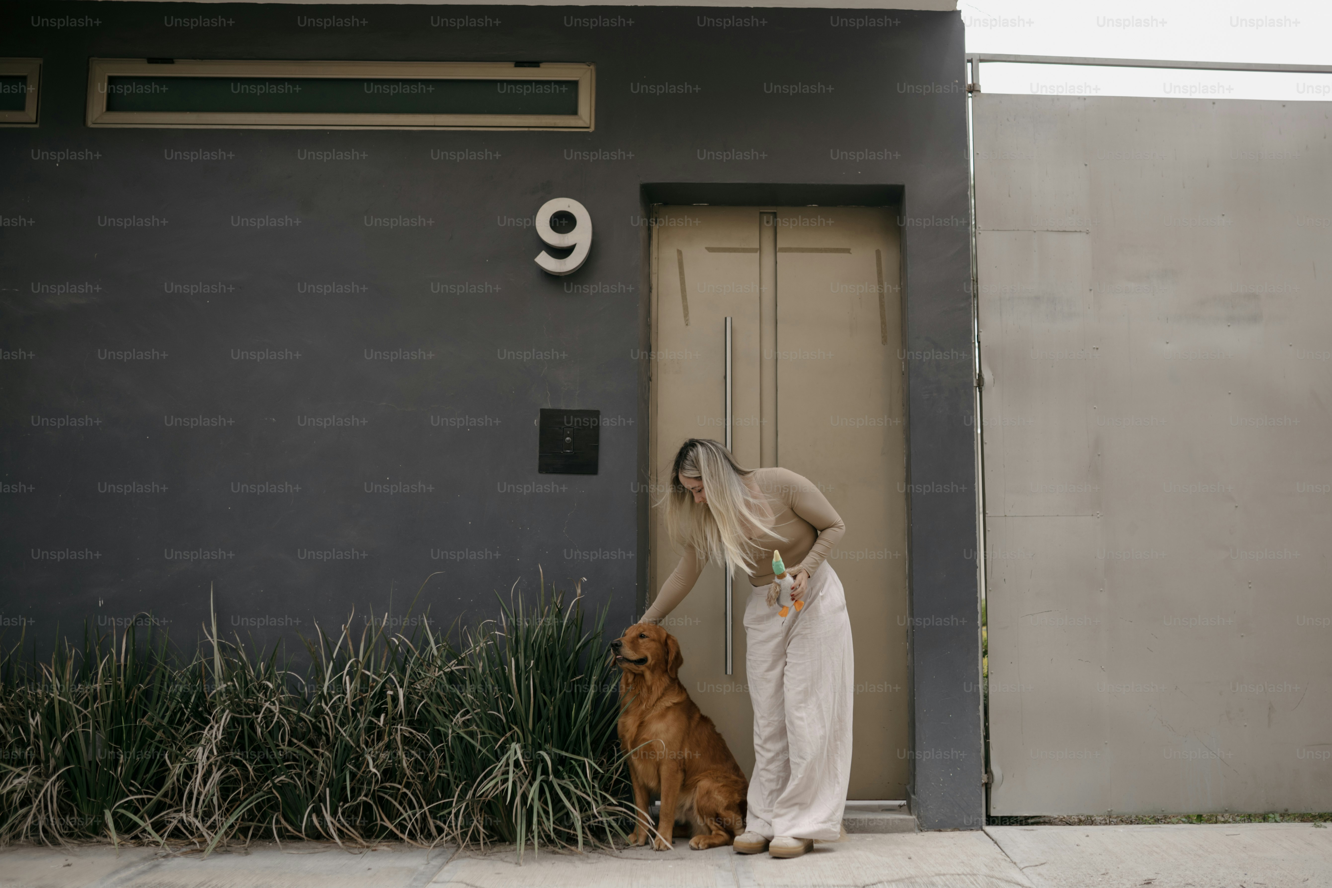 Woman petting a golden retriever dog outside a modern building.