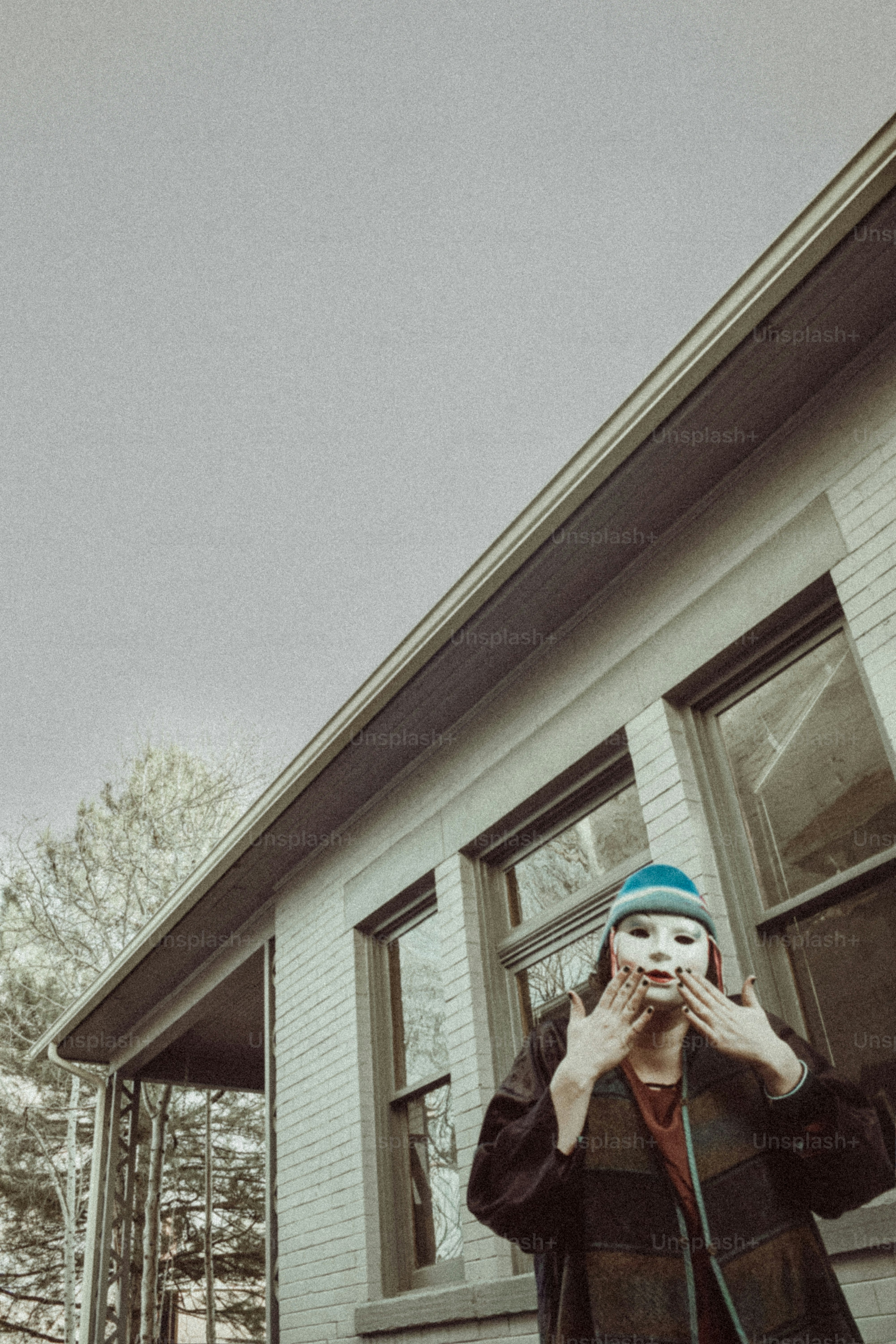 Person wearing mask and beanie in front of house