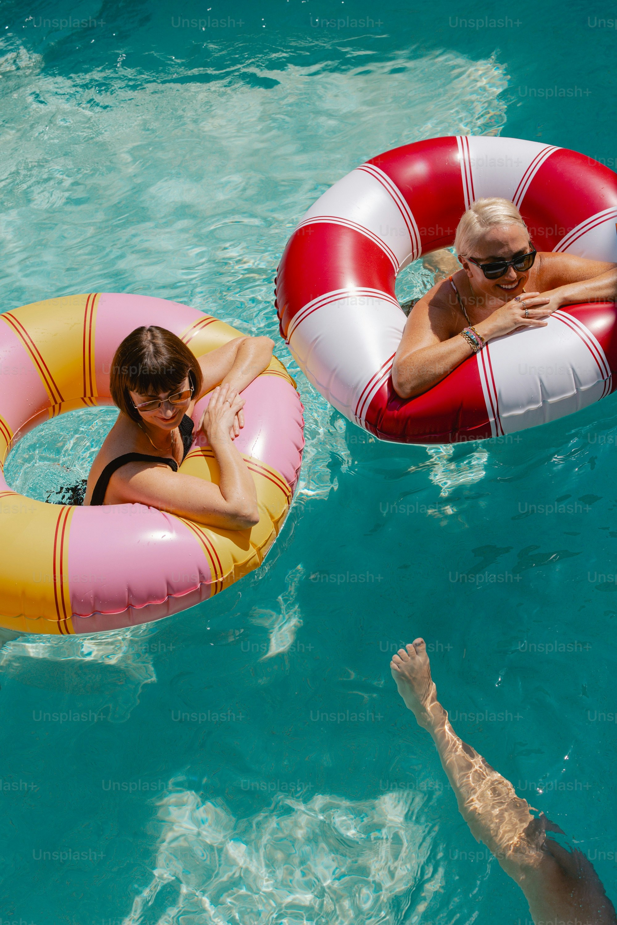 Two women float in a pool with inflatable rings.