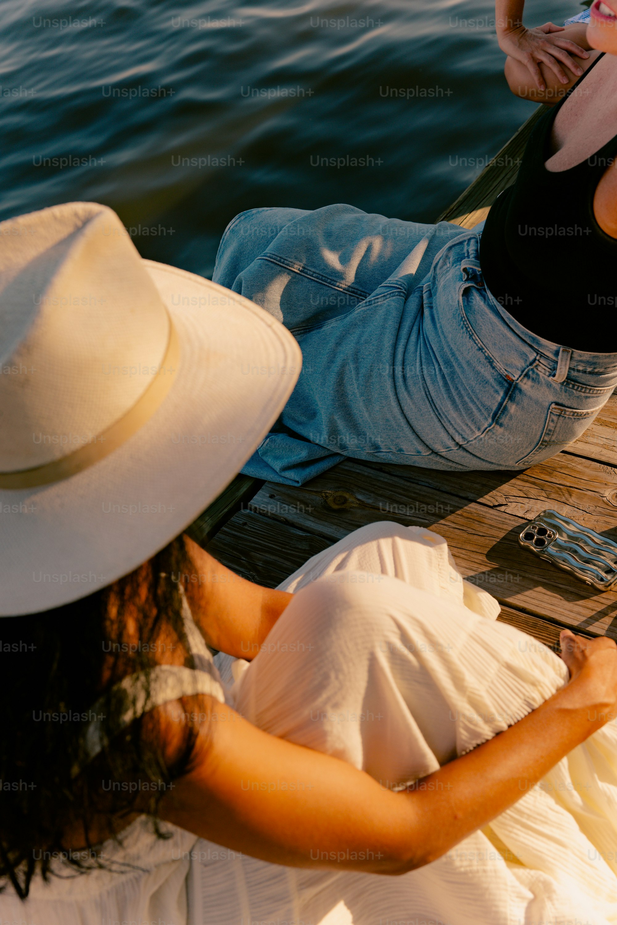 Two people sitting on a wooden dock by water