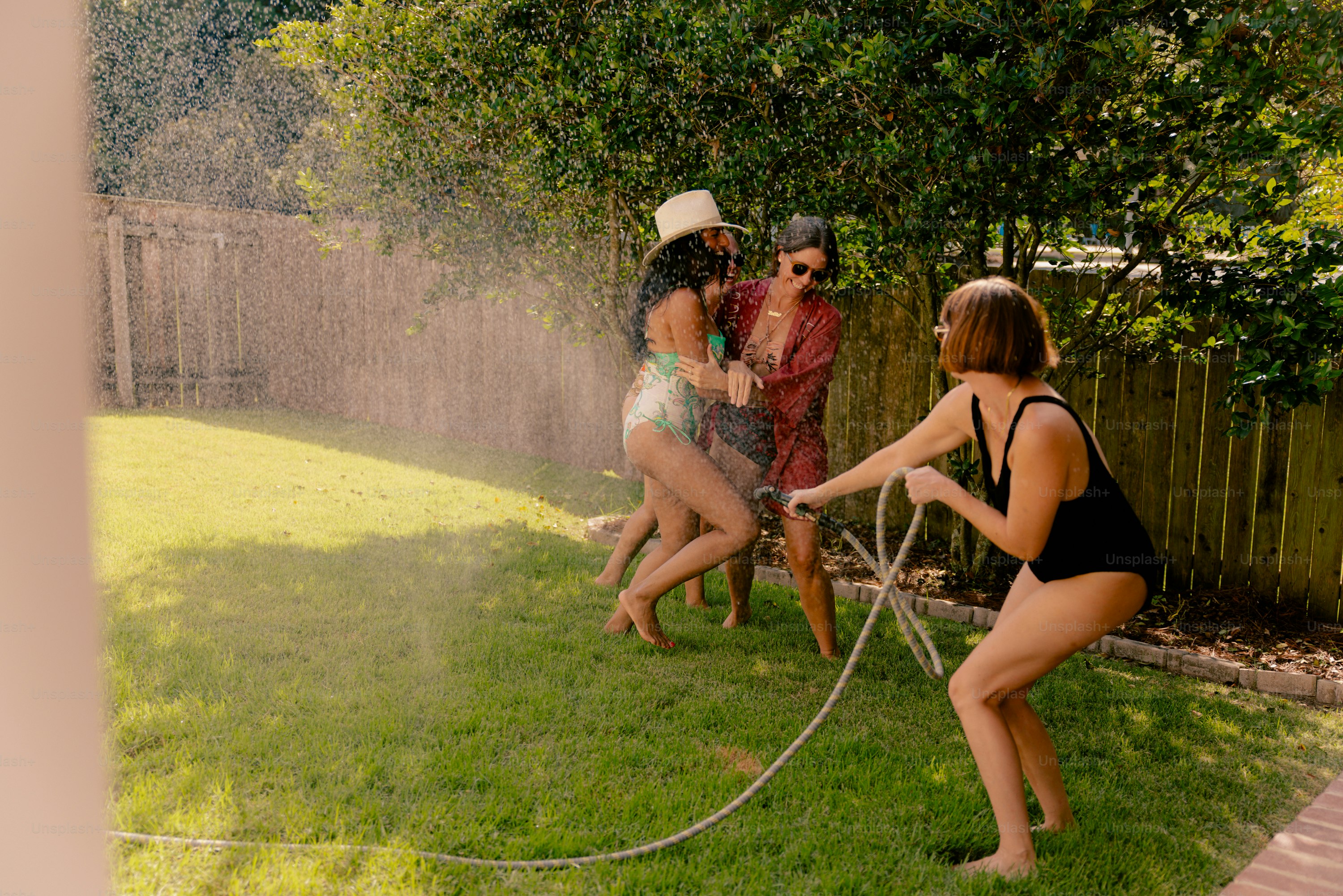 Mulheres brincando umas com as outras com uma mangueira de jardim