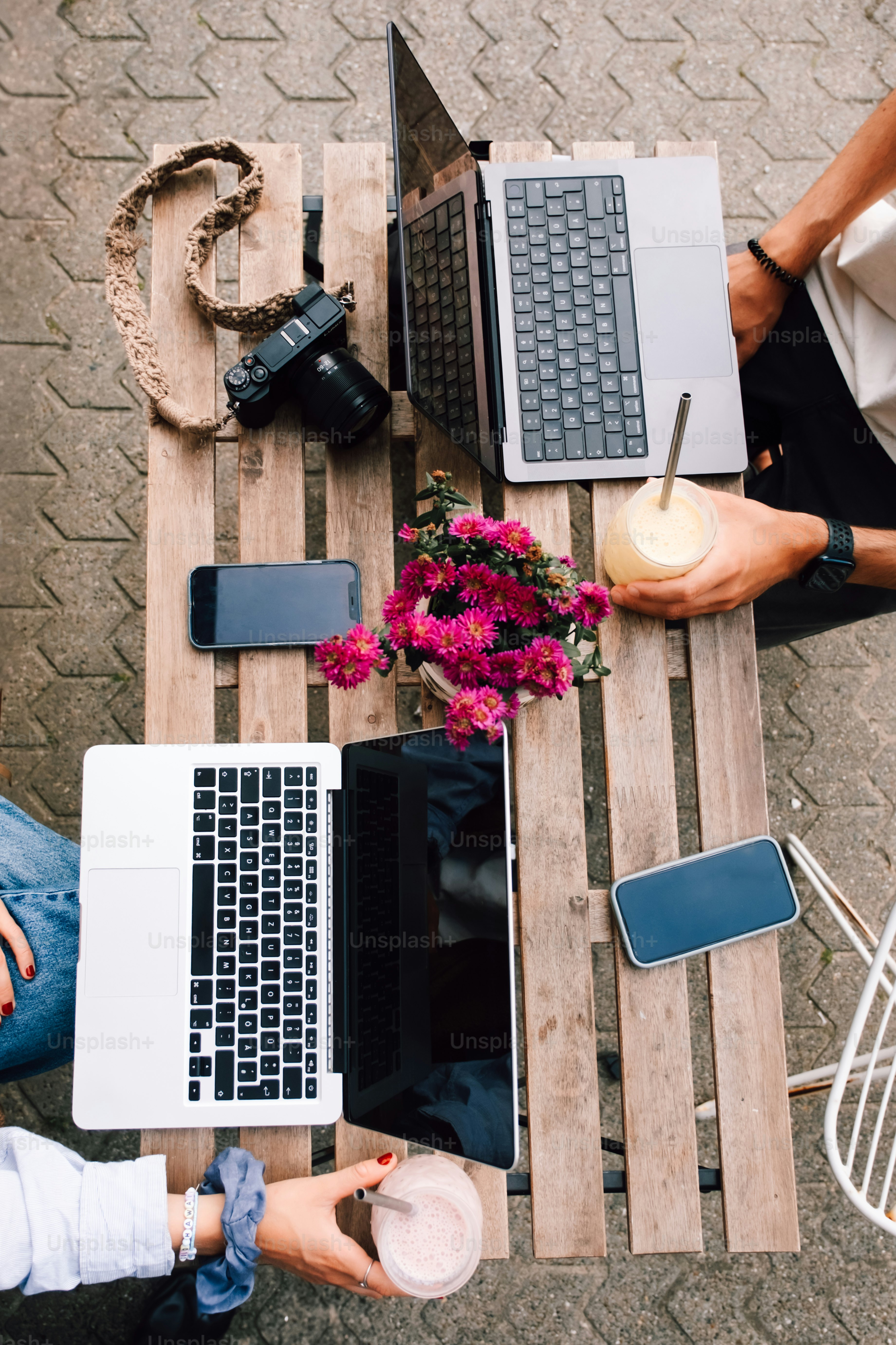 Two laptops, phones, camera, and drinks on table.
