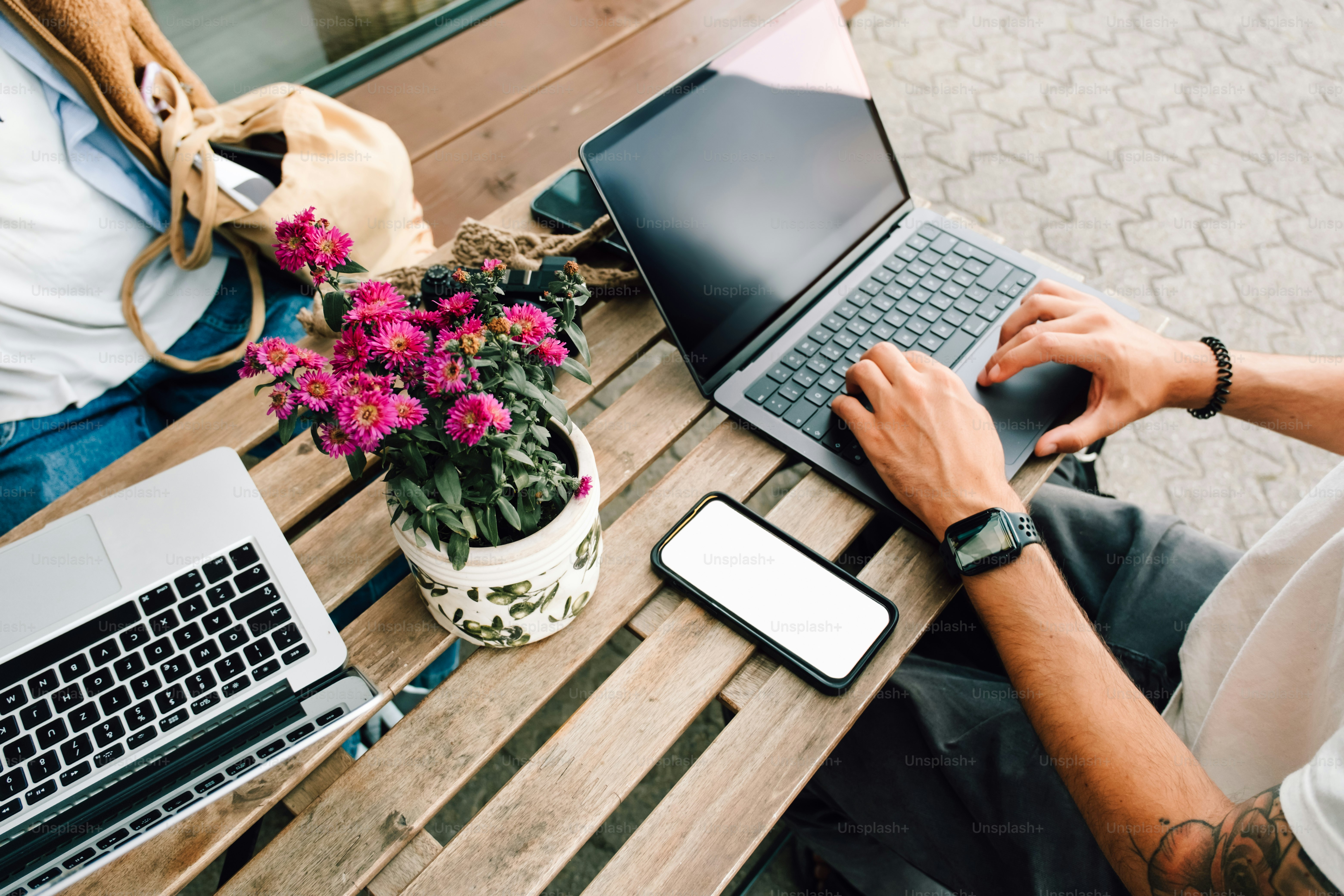 Two laptops and phone on wooden table with flowers