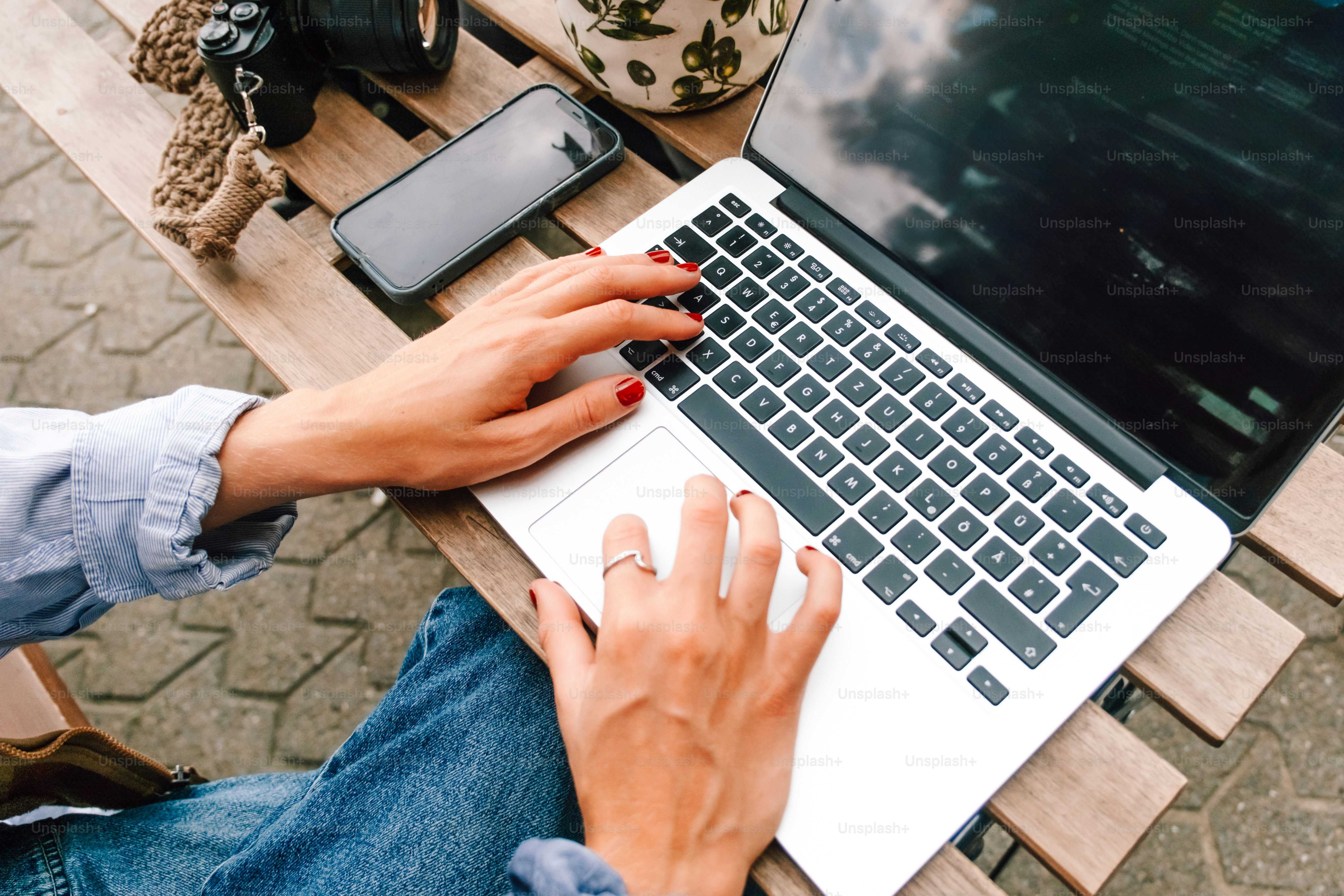 Person typing on a laptop outdoors at a wooden table.