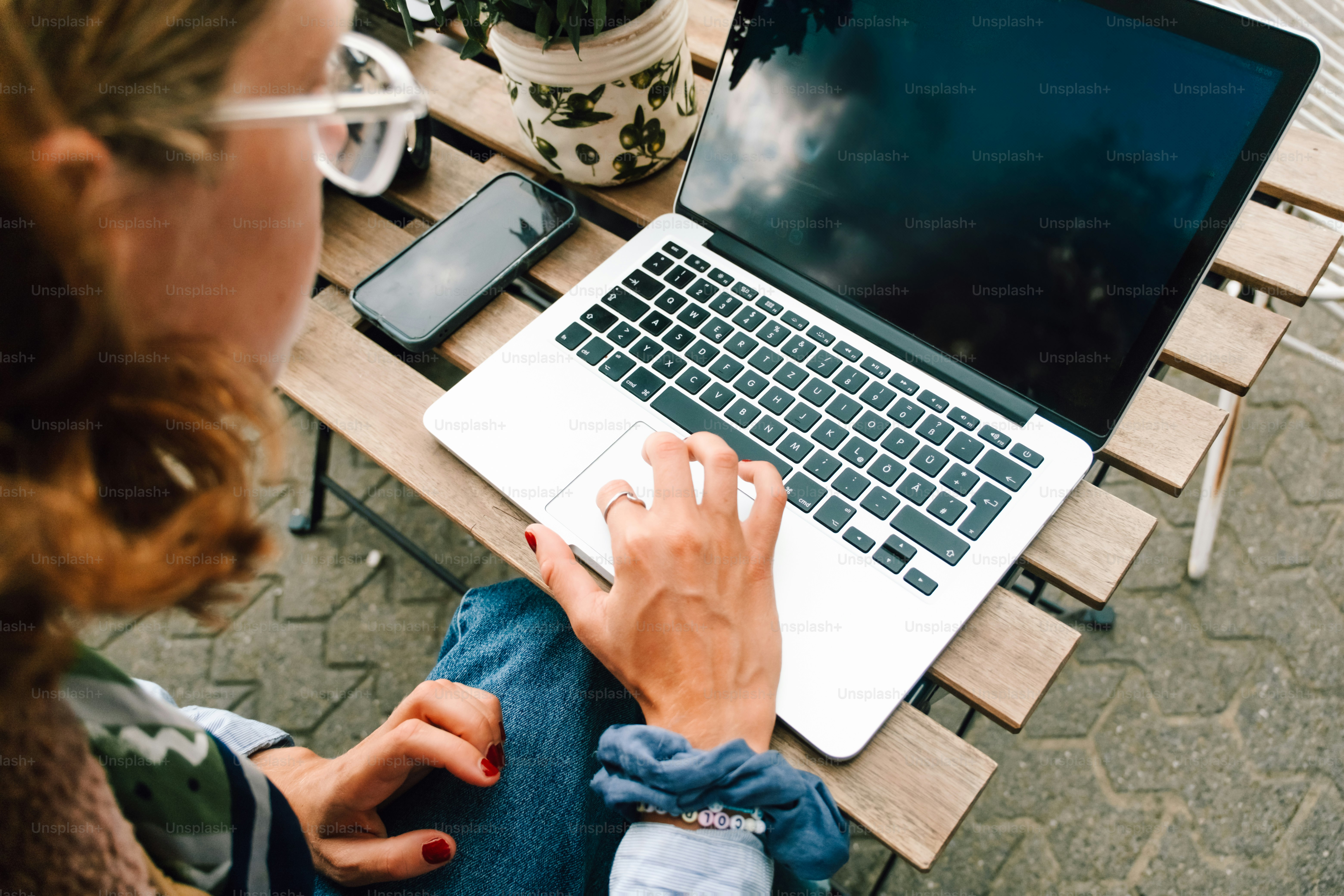 Woman working on a laptop at an outdoor table.